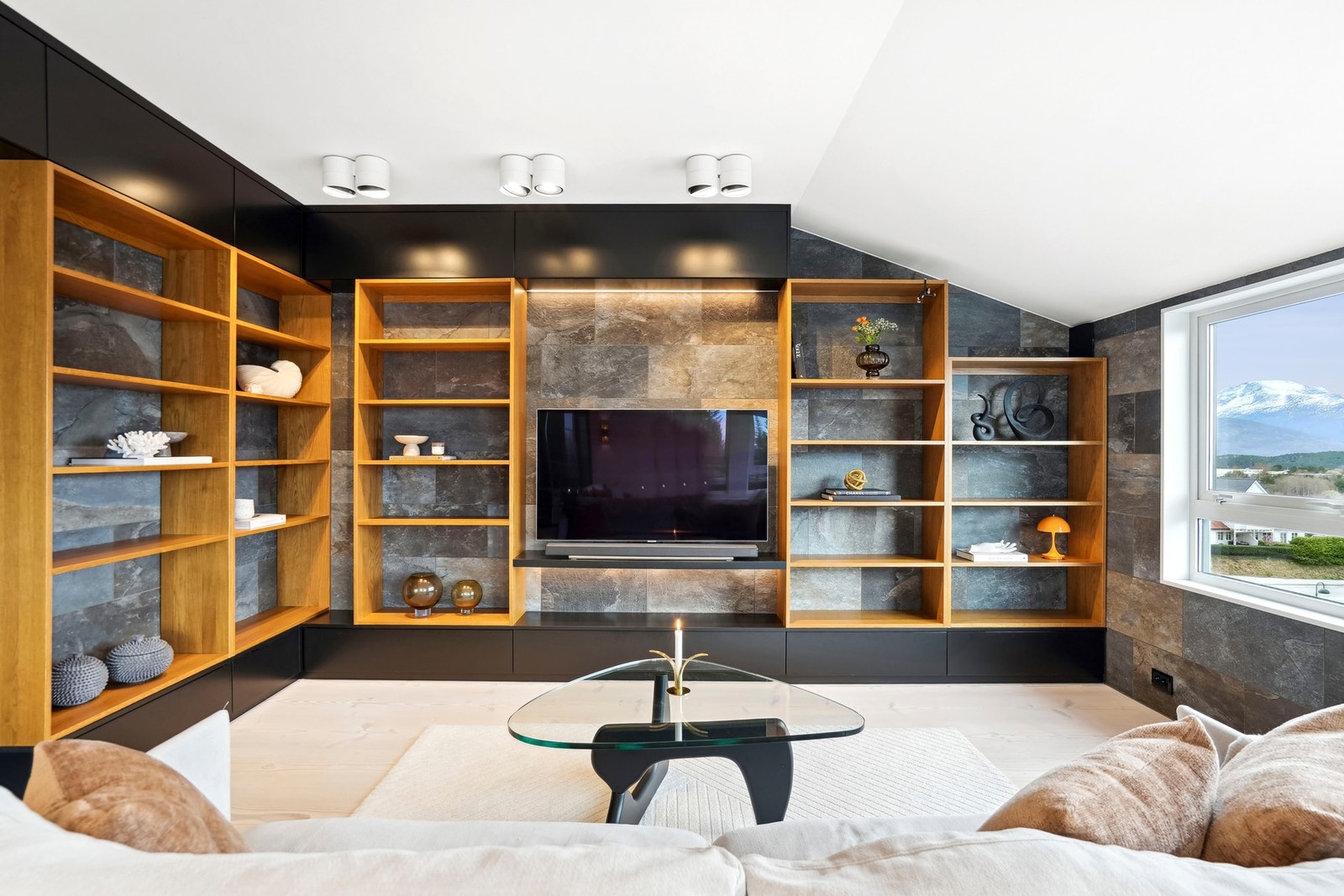 Langs to av veggene er det en snekkerbygd bokhylle med trehvite, åpne hyller, sorte skap, integrert belysning og nisje til flatskjerm. Galleribilde