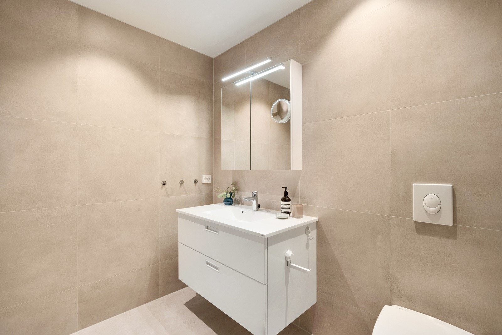Badet har dusjhjørne, vegghengt toalett, moderne innredning og spotter i tak. Varmekabler i gulv. Galleribilde