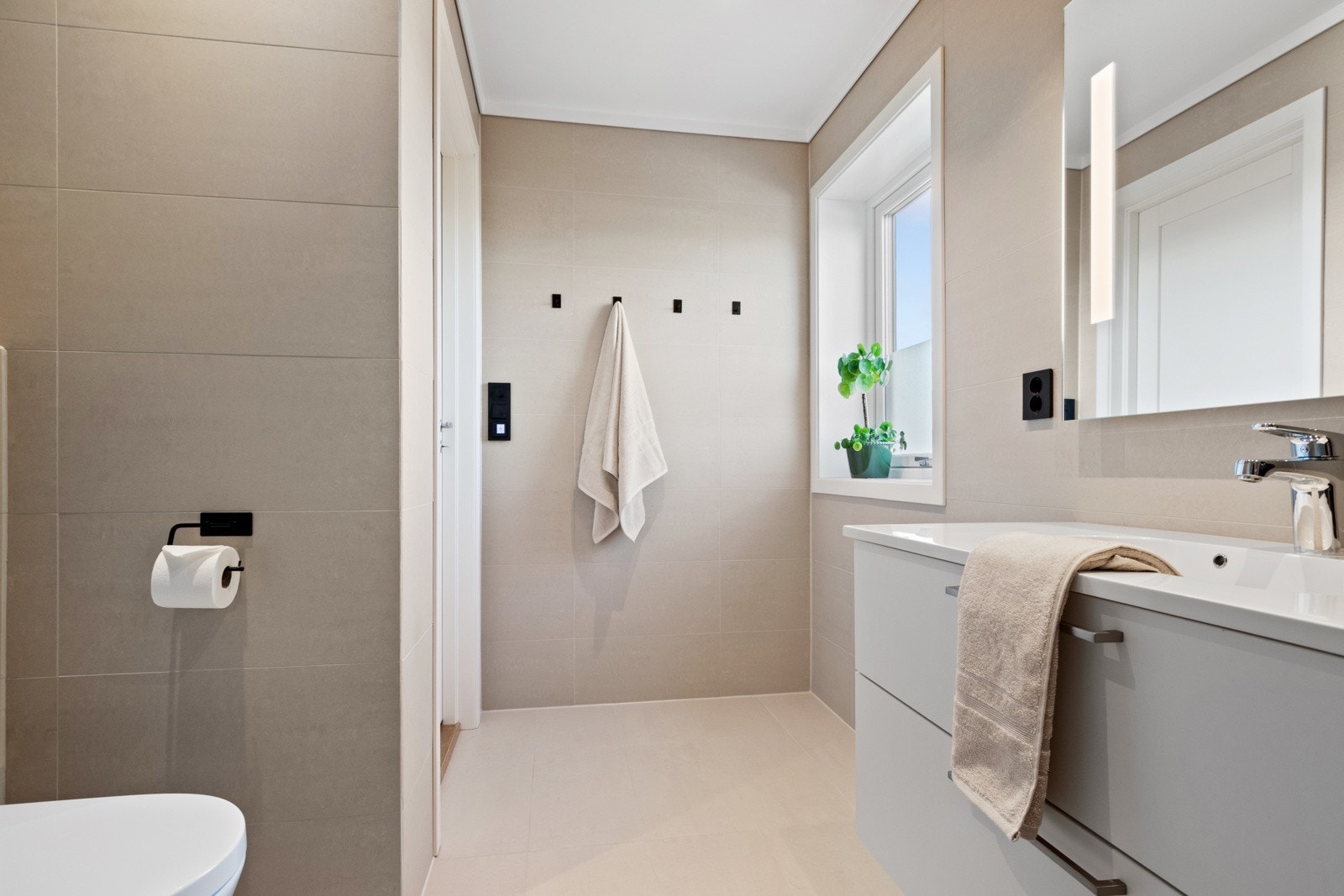 Baderomsinnredningen har hvite, glatte fronter og består av en heldekkende servant på en skapseksjon og et speil med integrert belysning. Galleribilde