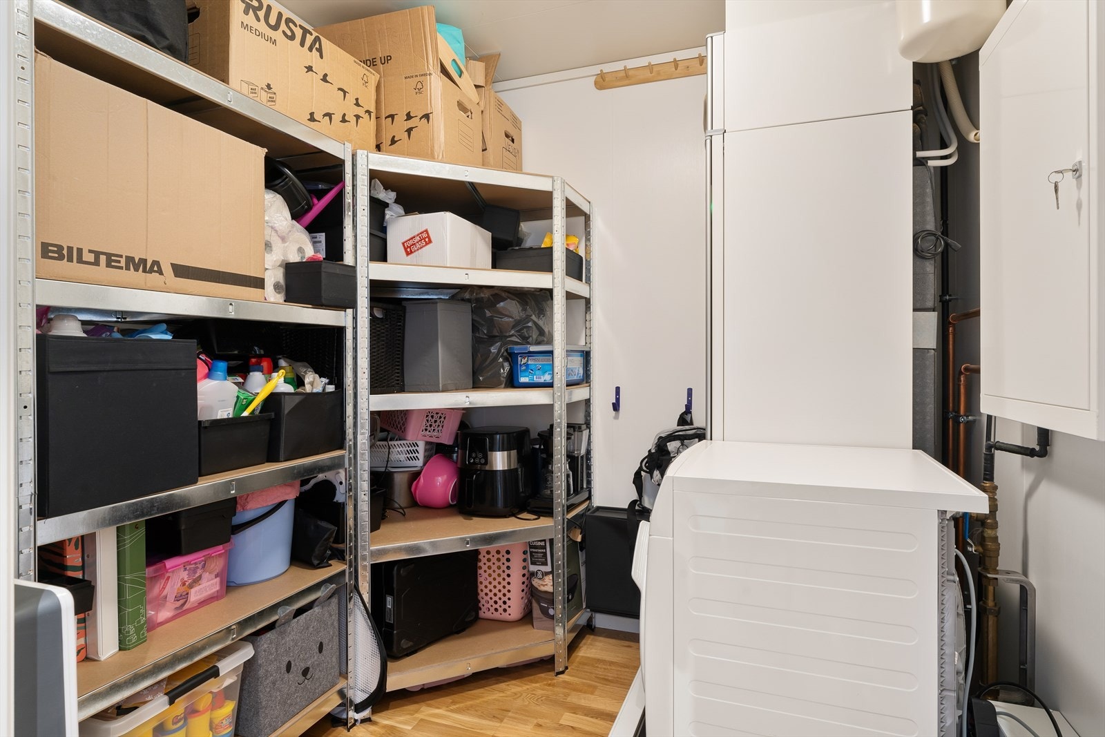 Romslig innvendig bod med både parkett og fliser på gulv. Her har man god lagringsplass, samt plass til både vaskemaskin og tørketrommel Galleribilde