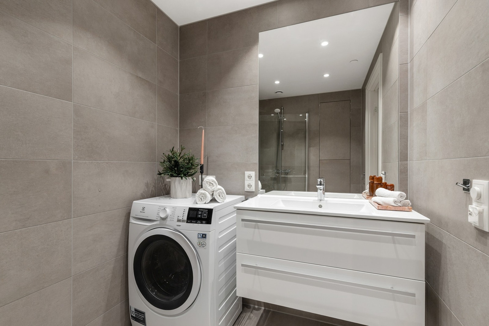 Rommet er utsyrt med dusjhjørne med innfellbare dører, vegghengt toalett, servantinnredning med ovenpåliggende servant og opplegg for vaskemaskin Galleribilde