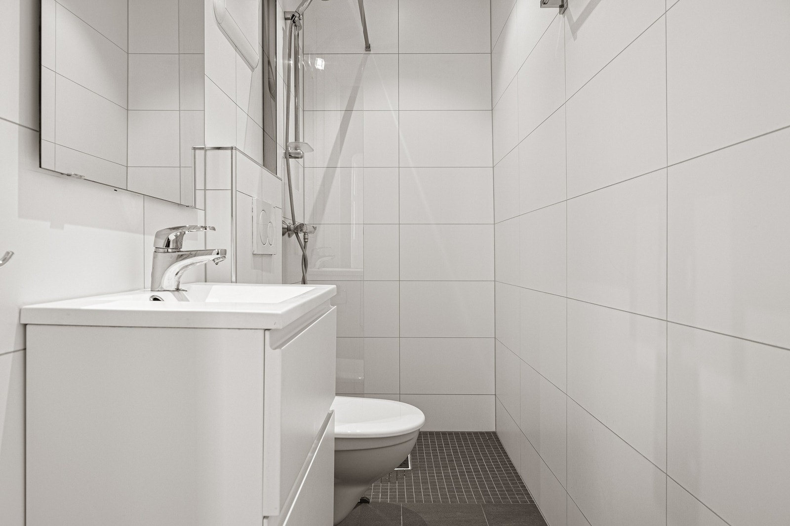 Fra entréen kommer man til det første badet som er på ca. 2,5 kvm. Her er det god belysning med downlights. Badet inneholder dusj med glassvegg, servant med oppbevaring og vegghengt toalett. Galleribilde