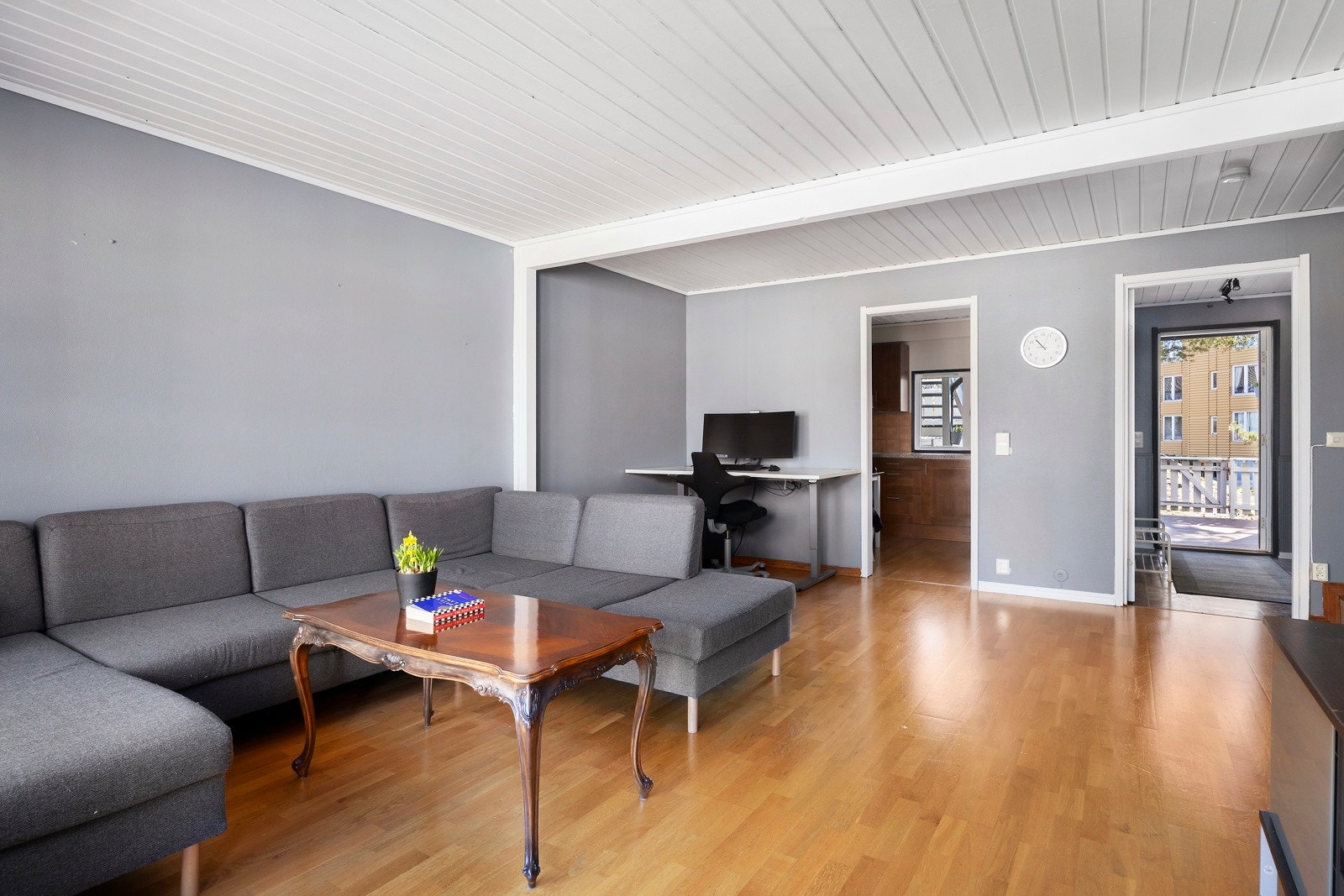 Romslig stue med grå vegger, parkettgulv og god plass til sofagruppe. Innenforliggende separat kjøkken. Galleribilde