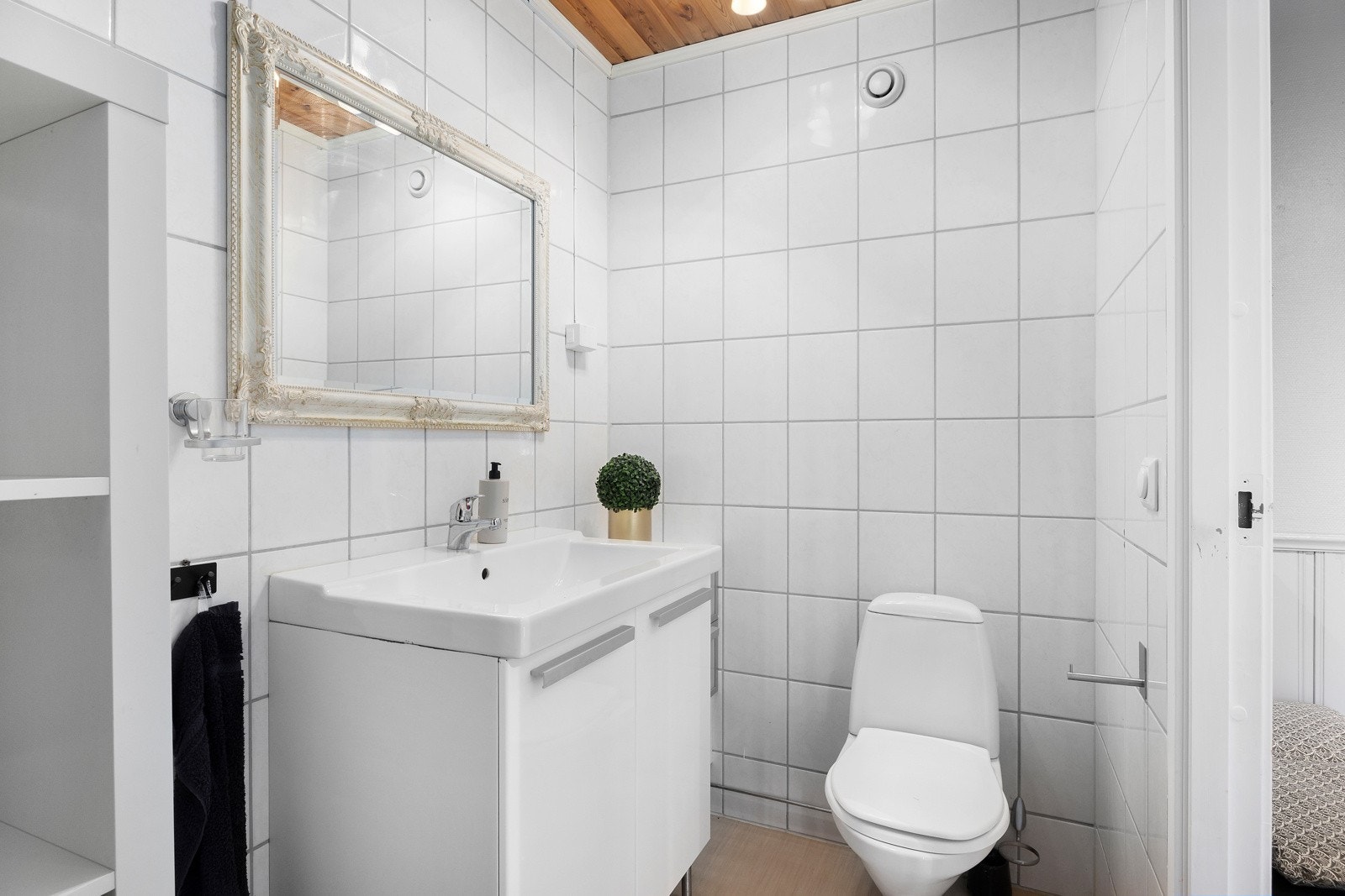 Toalettrom med hvite fliser, servant med underskap og vegghengt speil. Galleribilde