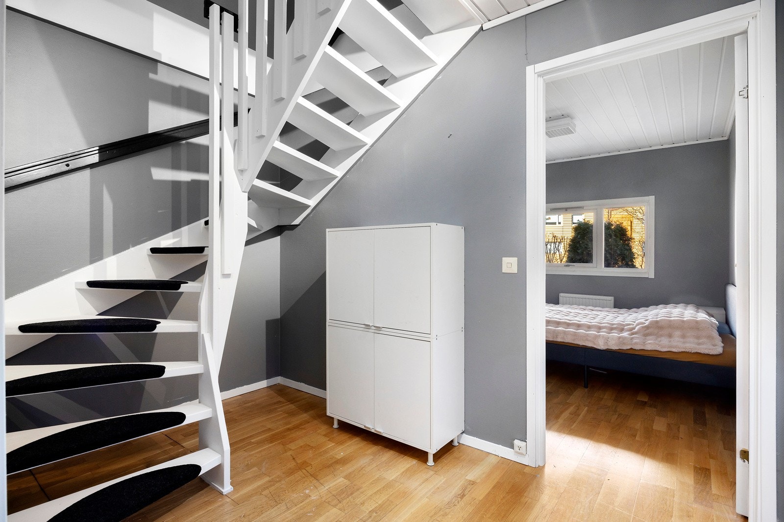 Nylig malt hvit trapp, grå vegger, lys parkett og adkomst til soverom med vindu. Galleribilde