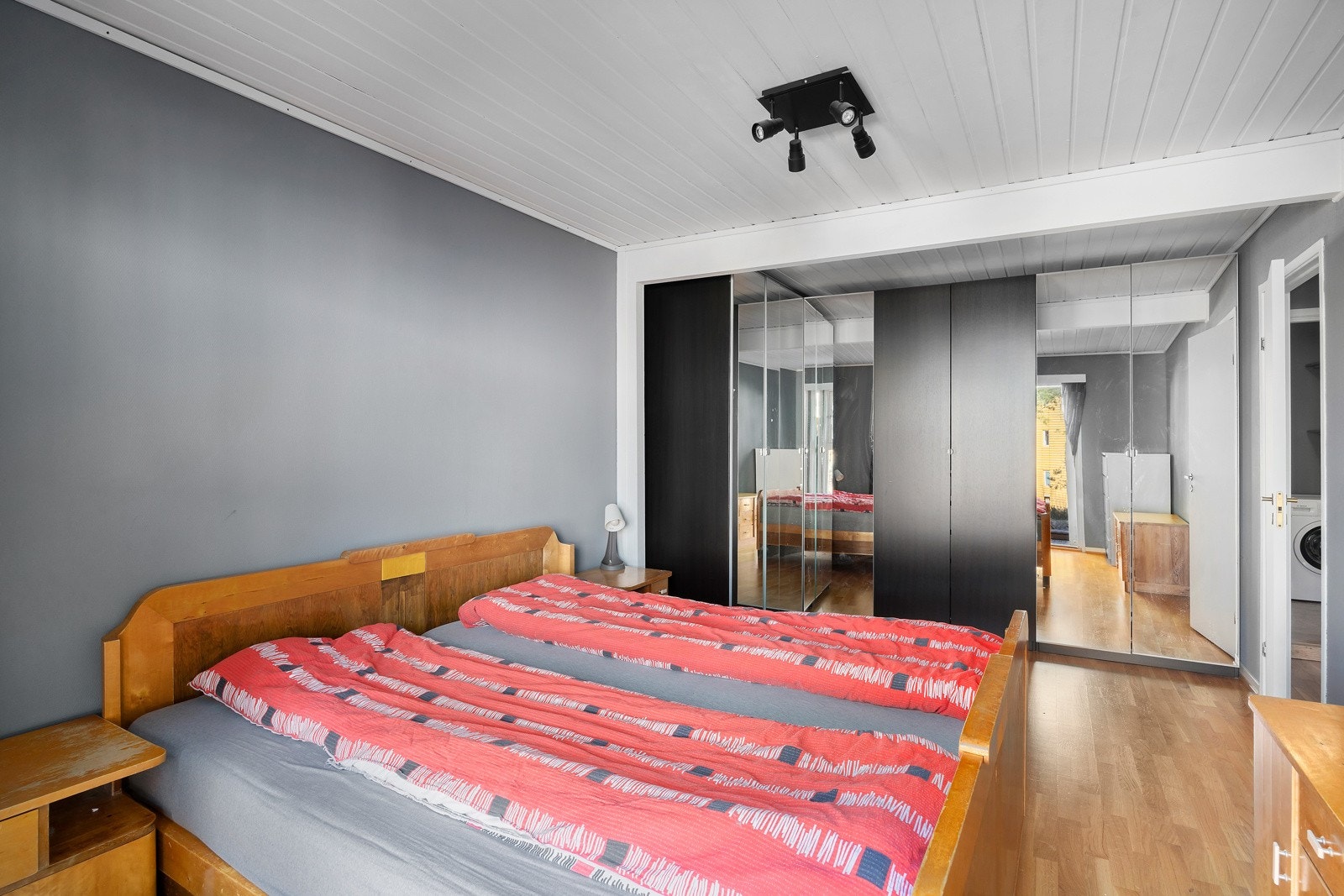 Soverom med god plass til dobbeltseng, speilskap og grå vegger. Lys takpanel og parkettgulv. Galleribilde