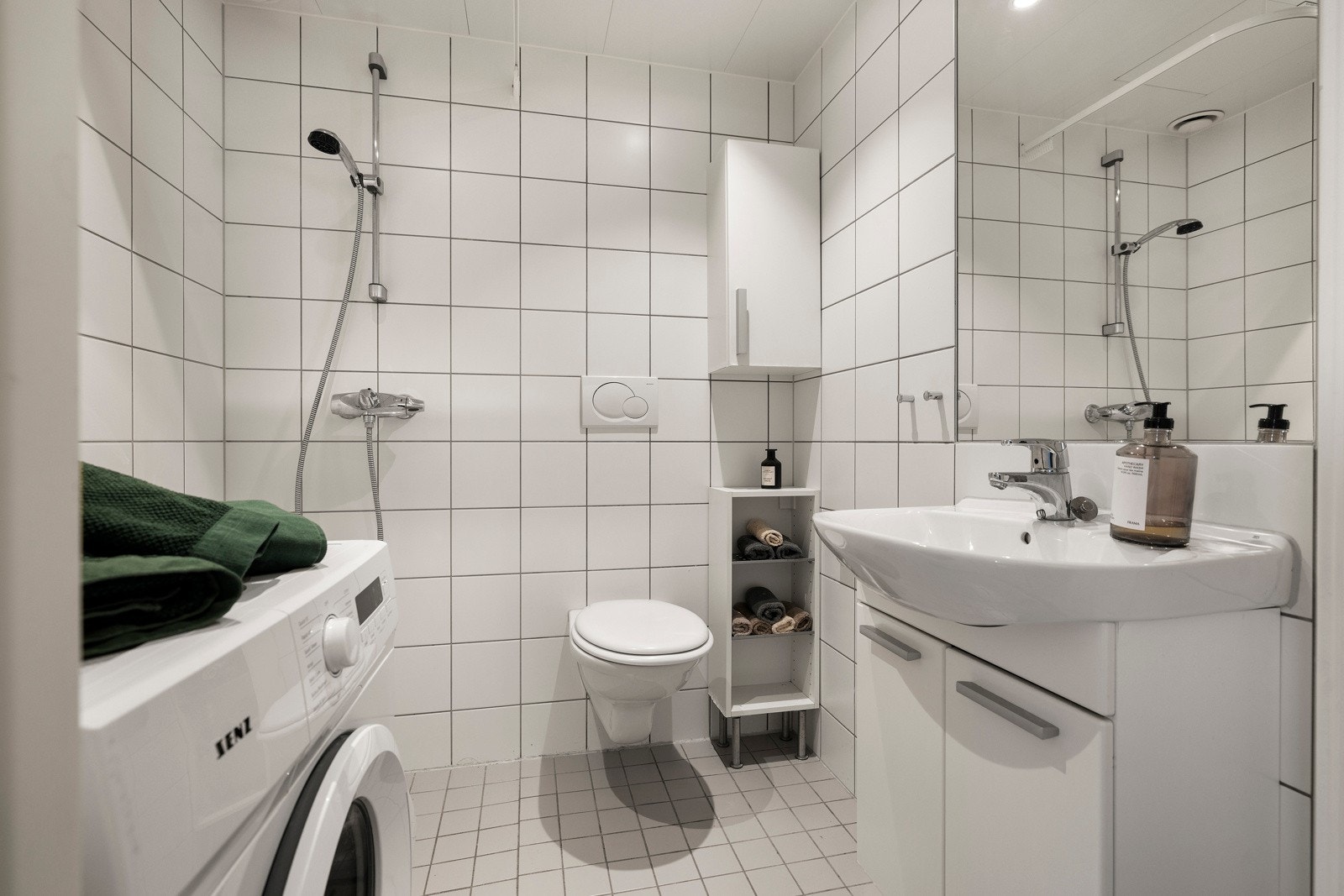 Lyst bad med hvite fliser og opplegg for vaskemaskin Galleribilde