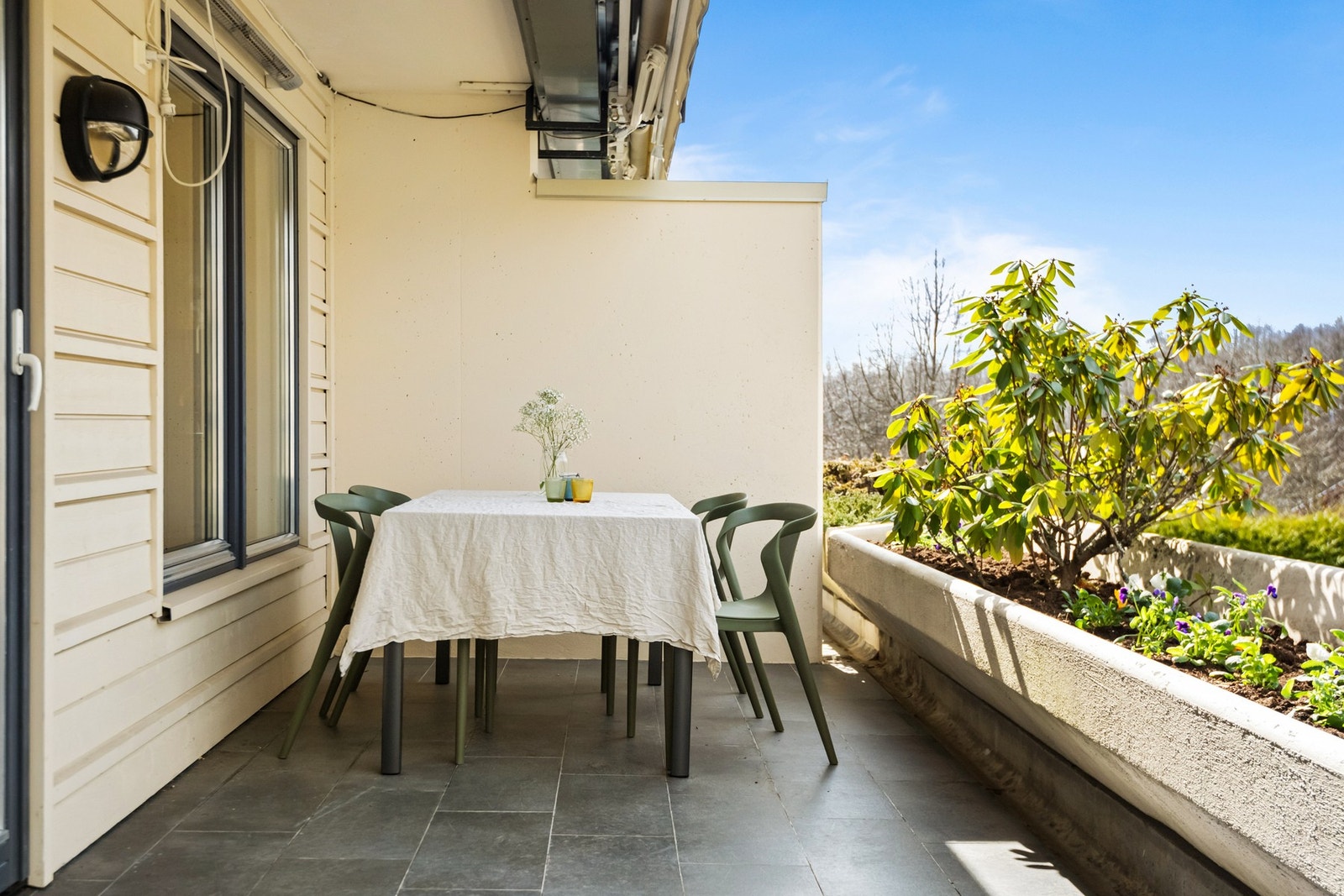 Balkongen har gulv av betong belagt med fliser og rekkverk av metall og glass med blomsterkasse. Galleribilde
