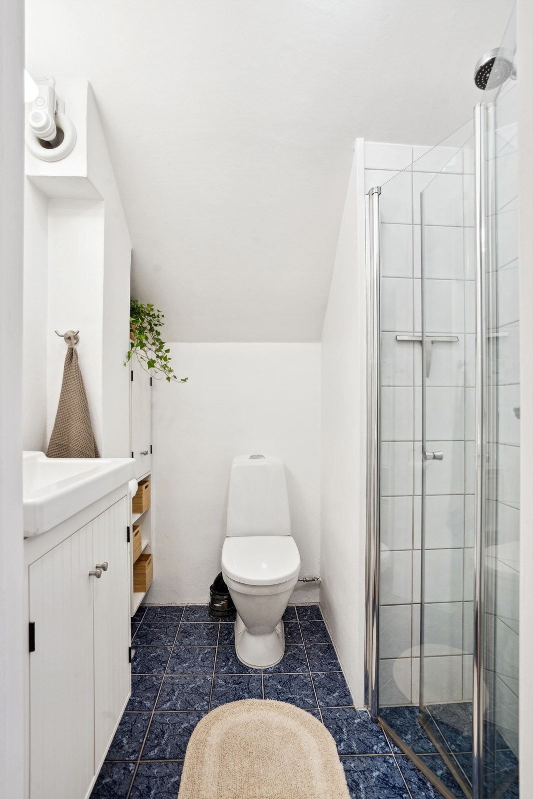 Badet inneholder toalett, dusjnisje og vask med skapinnredning. Det er også skap i hjørnet for ekstra oppbevaringsplass Galleribilde