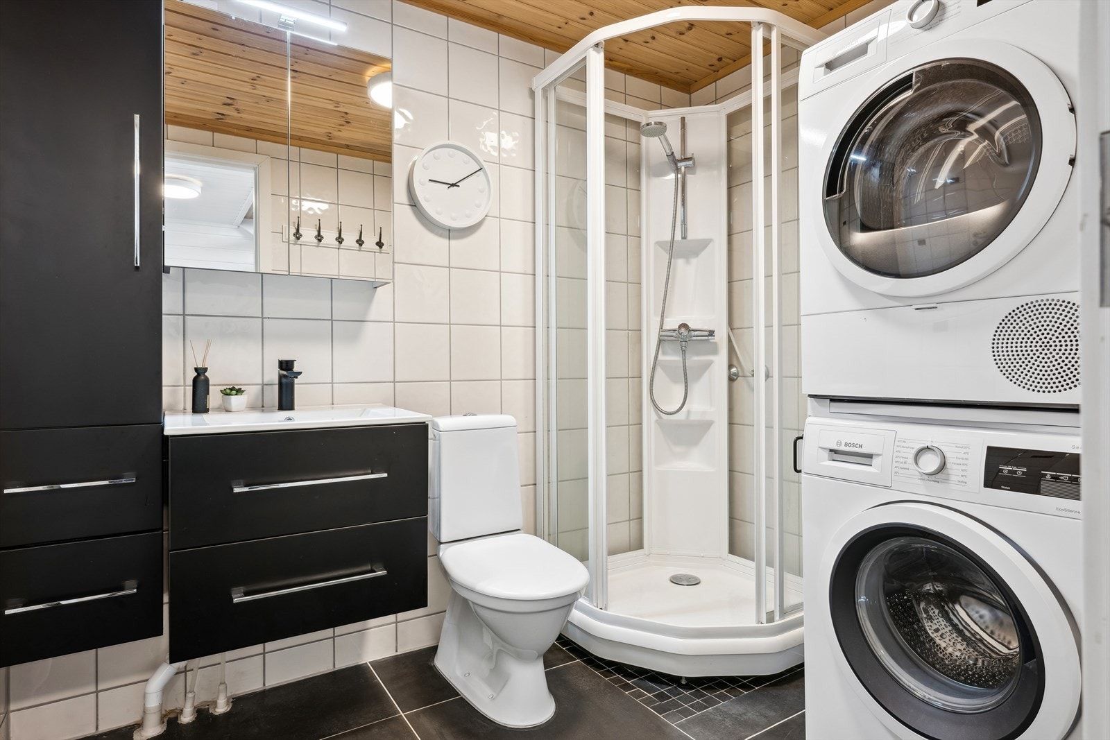 Delikat flislagt bad/vaskerom med dusjkabinett, wc, moderne baderomsinnredning og opplegg for vaskemaskin/tørketrommel. Galleribilde