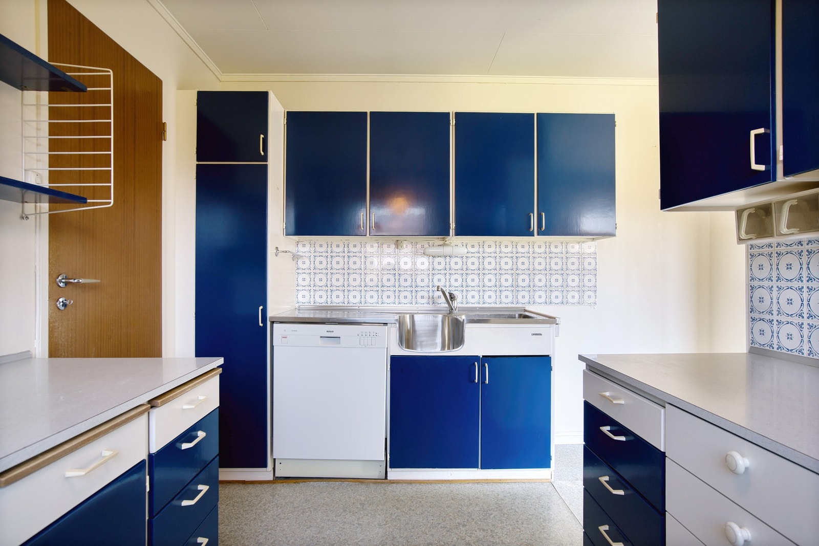 Kjøkkenet har en eldre standard med malt innredning og benkeplate i stål og laminat Galleribilde