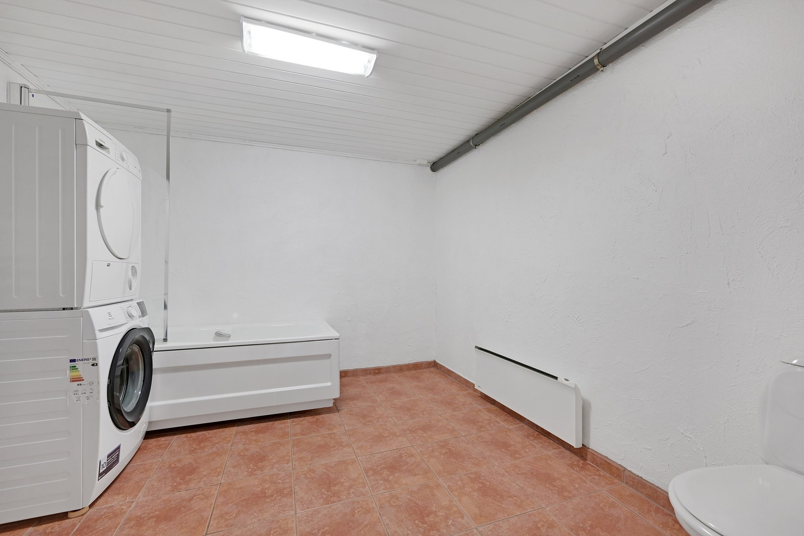 Vaskerom med toalett, badekar, opplegg for vaskemaskin og tørketrommel. Varmtvannsbereder er plassert i dette rommet. Galleribilde