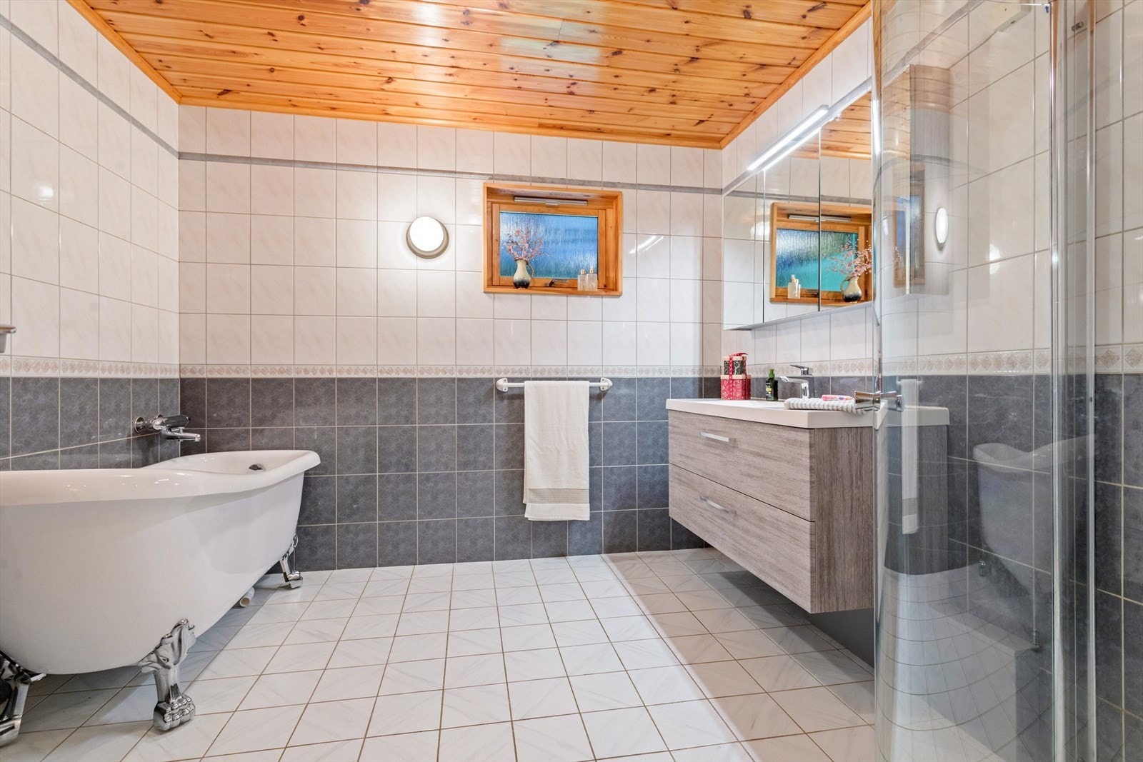 Baderommet er helfliset og har varmekabler i gulv. Det er utstyrt med dusjhjørne, servant med tilhørende servantskap, toalett og badekar. Galleribilde
