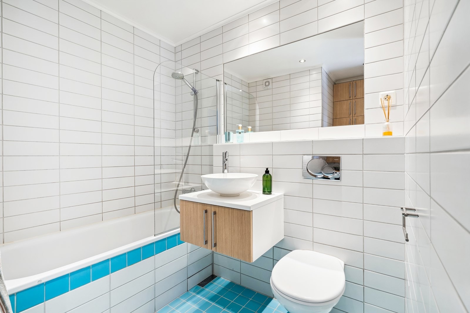 Helfliset bad med varmekabler i gulv. Innfliset badekar, vegghengt toalett og servant i møblement med oppbevaring. Galleribilde