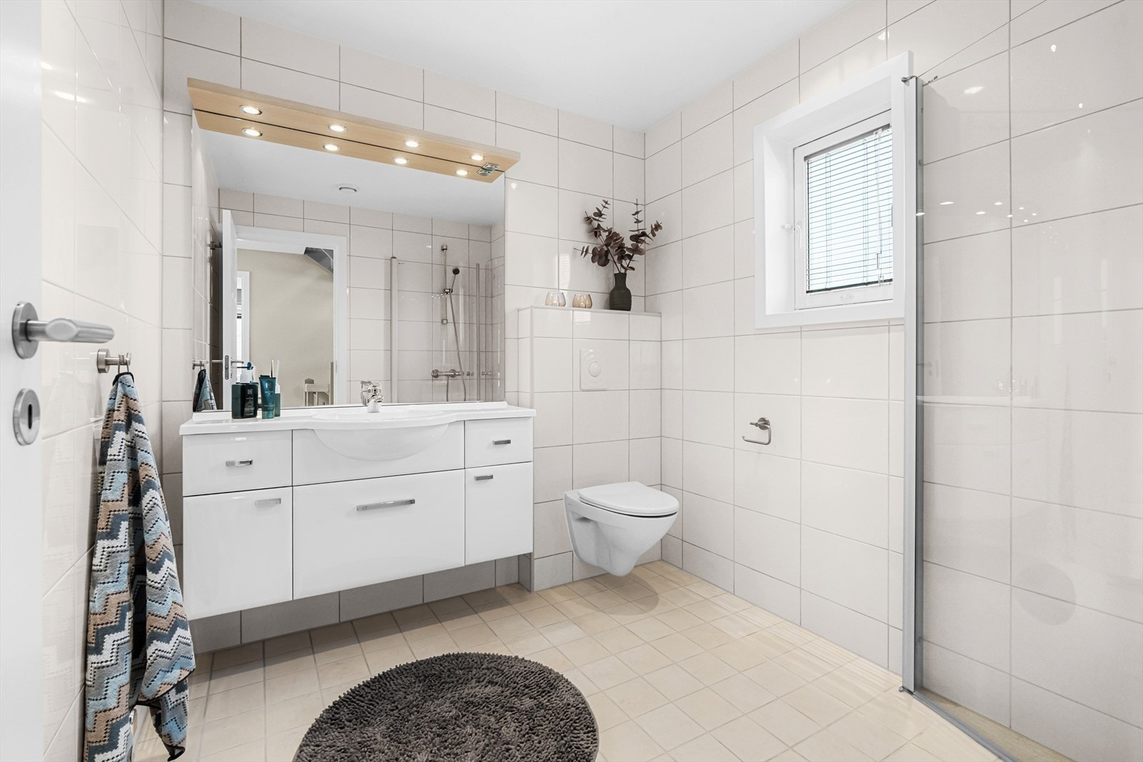 Hovedetasjen har også et stort, flislagt baderom med elektrisk gulvvarme og downlights i himlingen. Badet er innredet med vegghengt klosett, servant nedfelt i innredning, speil med lys og dusjhjørne med svingbare glassdører. Galleribilde