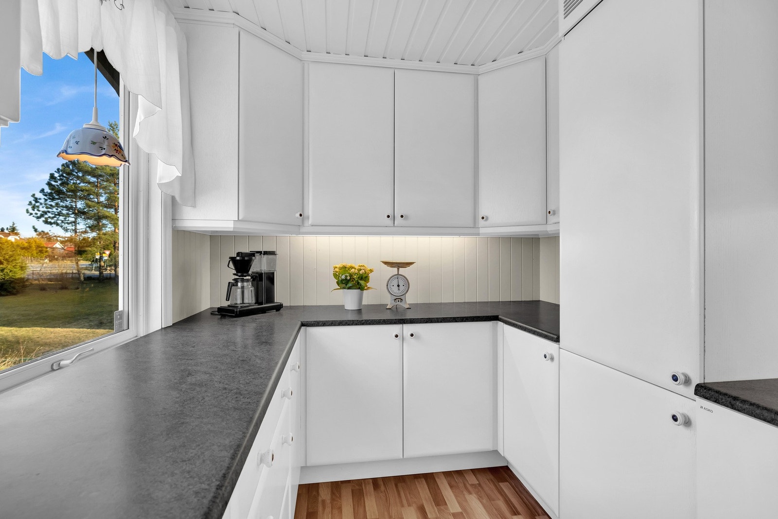 Mekanisk kjøkkenventilator er tilkoblet avtrekkskanal. Det er benkeskapsbelysning og stikkontakter under overskap som lyser opp arbeidsflatene. Galleribilde