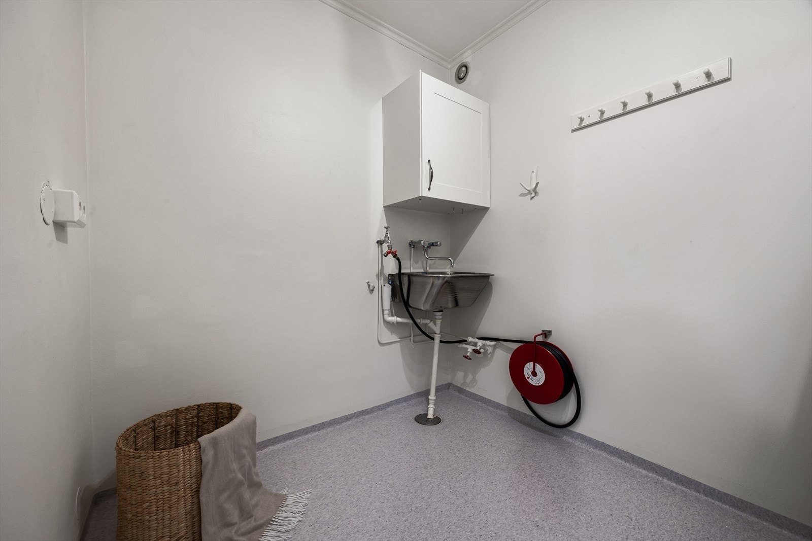 Vaskerommet har belegg på gulvet, malte veggflater og malt betong i himling. Rommet er utstyrt med opplegg for vaskemaskin, utslagsvask montert på vegg og praktisk skap over vask. Galleribilde