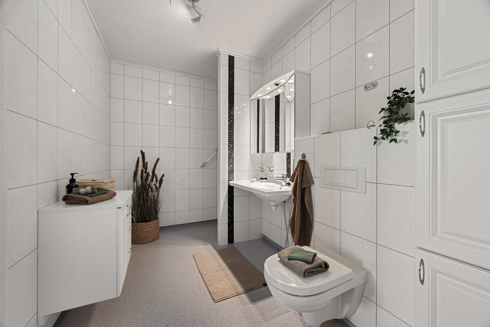 Badet er innredet med dusj, veggmontert toalett og servant, samt speilskap med belysning. Galleribilde