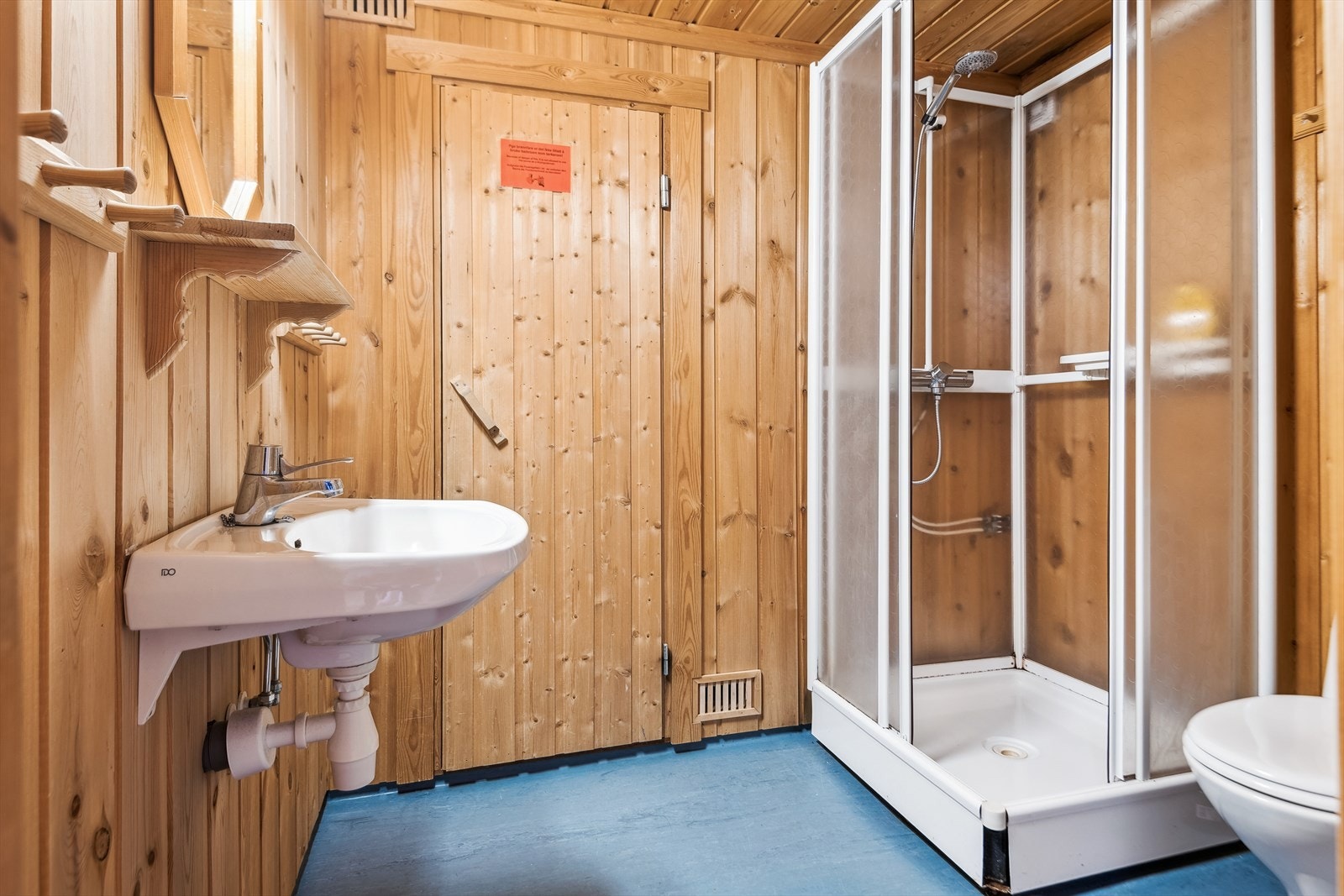 Badet er beliggende i enden avgangen og innredet med servant med ettgreps armatur, speil, hylle, knagger og for oppheng. Dusjkabinett med skyvedører i glass og gulvmontert toalett. Galleribilde