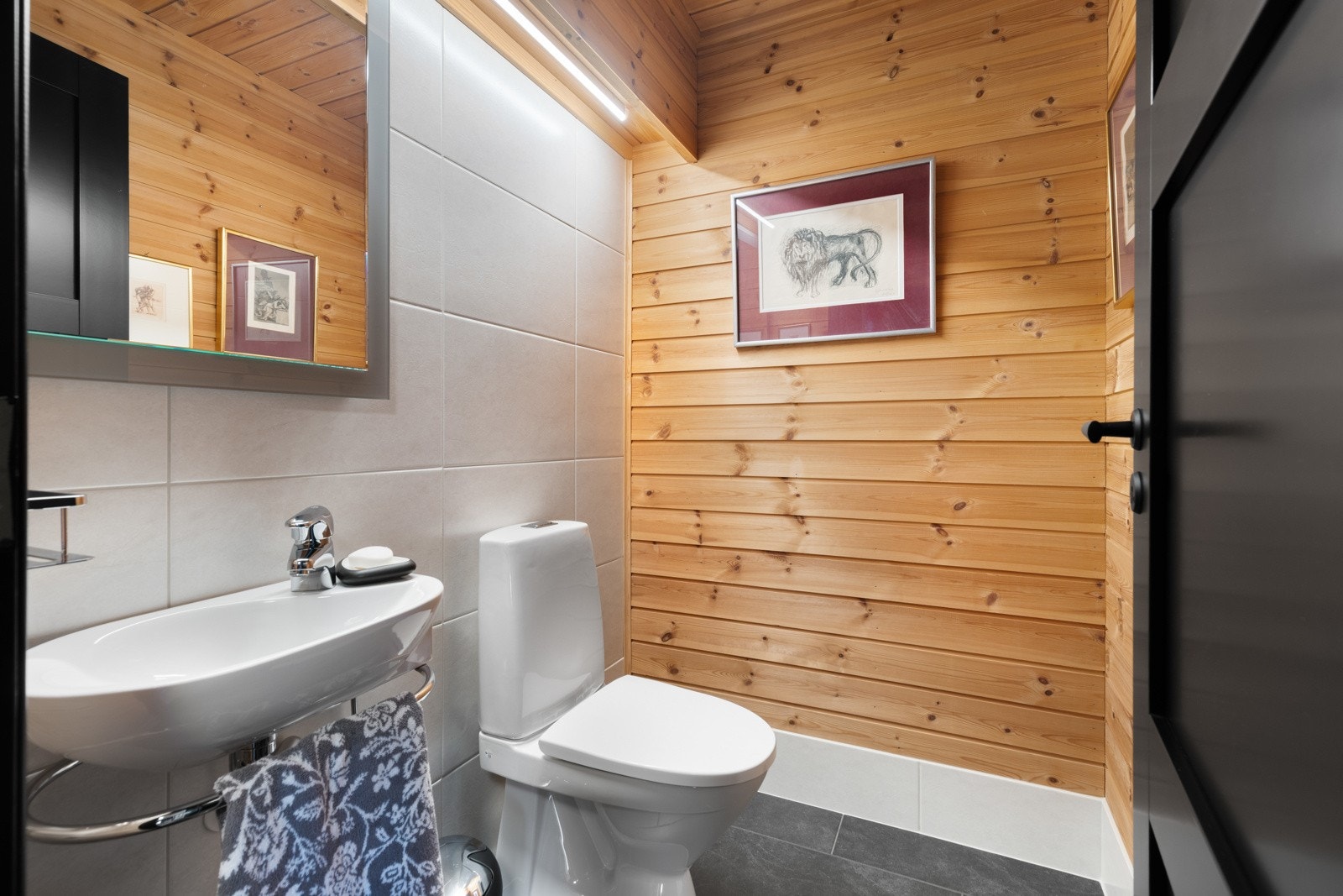 Wc-rommet har en kombinasjon av naturlig panel og hvite fliser på veggene, og det er koksgrå fliser på gulv med gulvvarme. Galleribilde