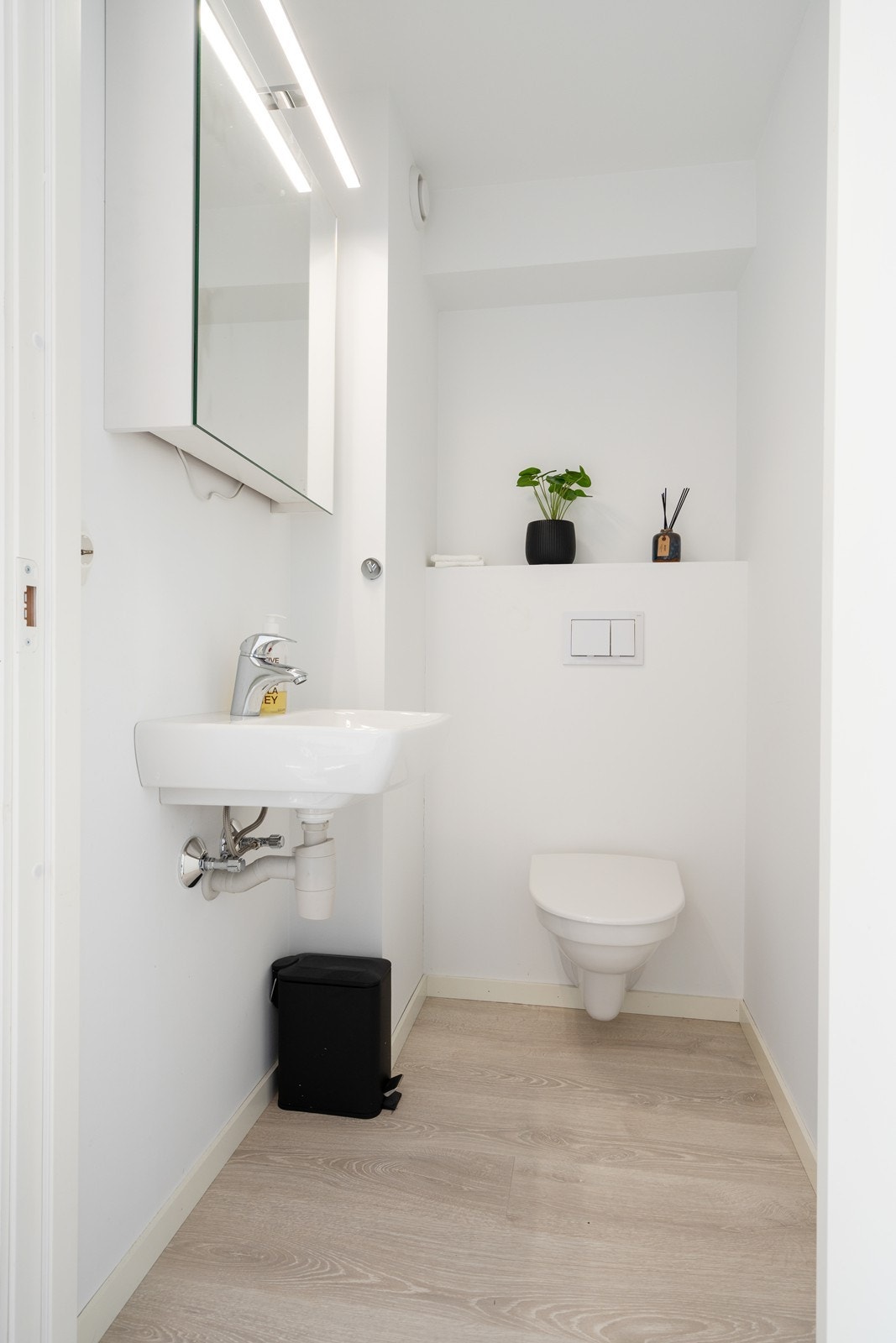 Pent toalettrom med vegghengt toalett, enkel servant og speilskap med belysning Galleribilde