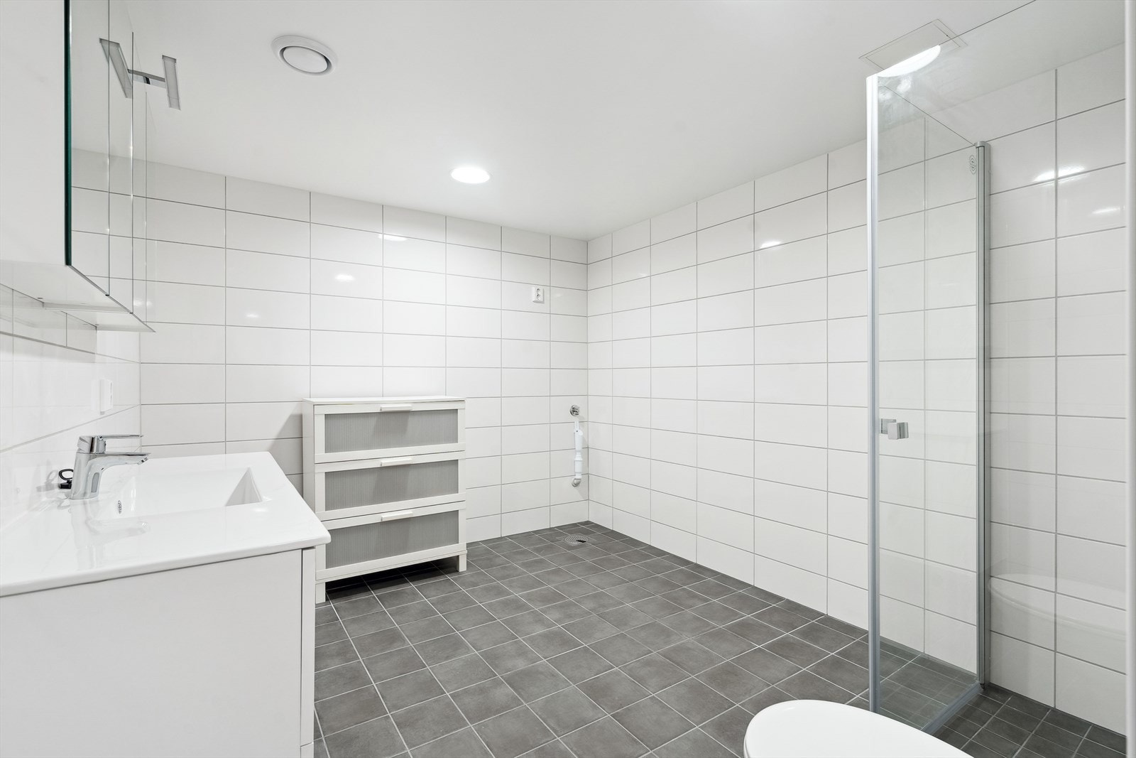 Varmekabler i gulv, vegghengt toalett, dusjdører, servantskap og opplegg for vaskemaskin. Galleribilde