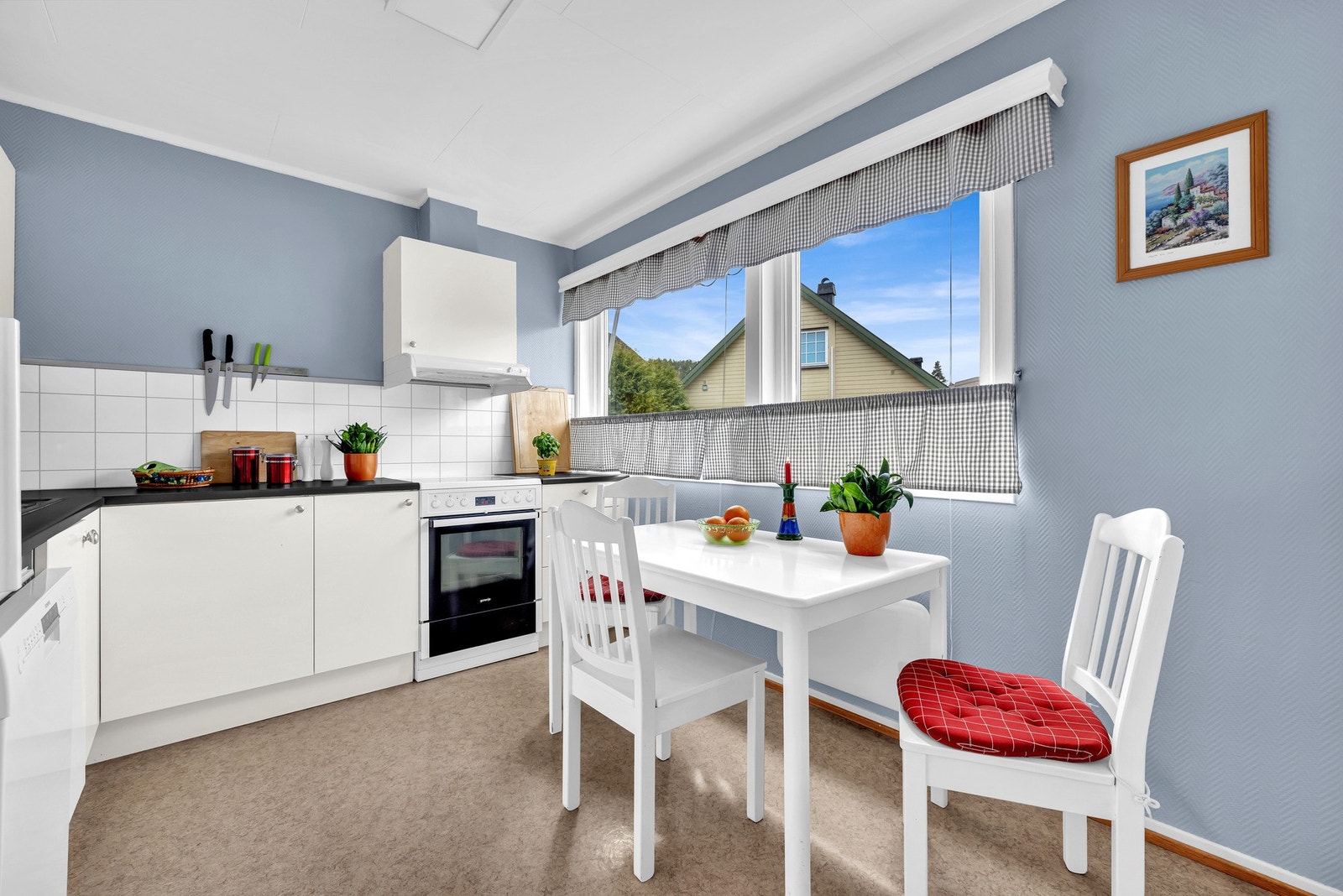 Kjøkkenet er utstyrt med en eldre kjøkkeninnredning med hvite glatte fronter, og laminert mørk benkeplate Galleribilde