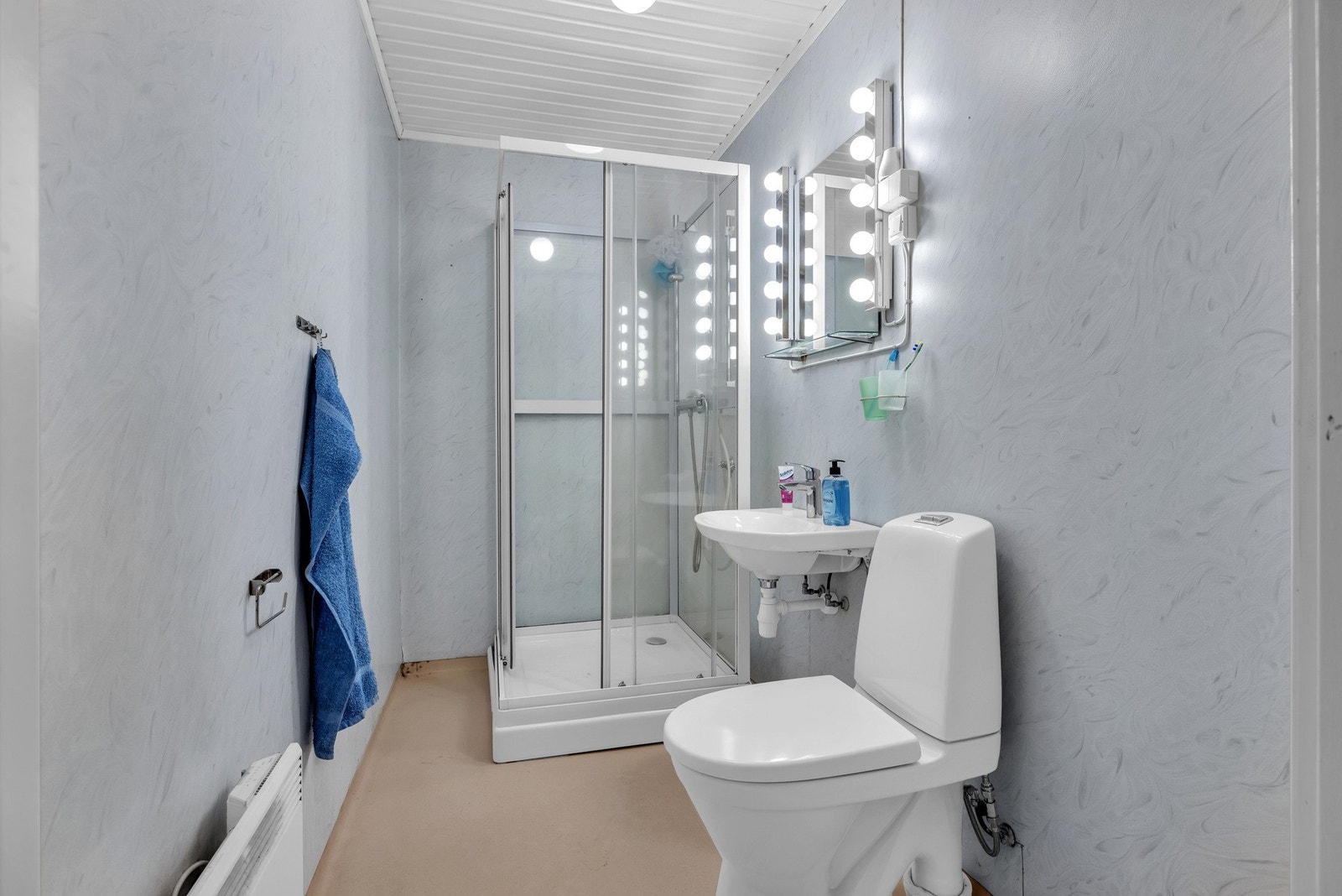 Badet i kjeller har samme standard som badet i 2. etg. og er også fra byggeår. Badet har gulvbelegg og våtromstapet, vegghengt servant med ett-greps armatur, dusjkabinett med glassdører, dusjarmatur og gulvmontert toalett. Galleribilde