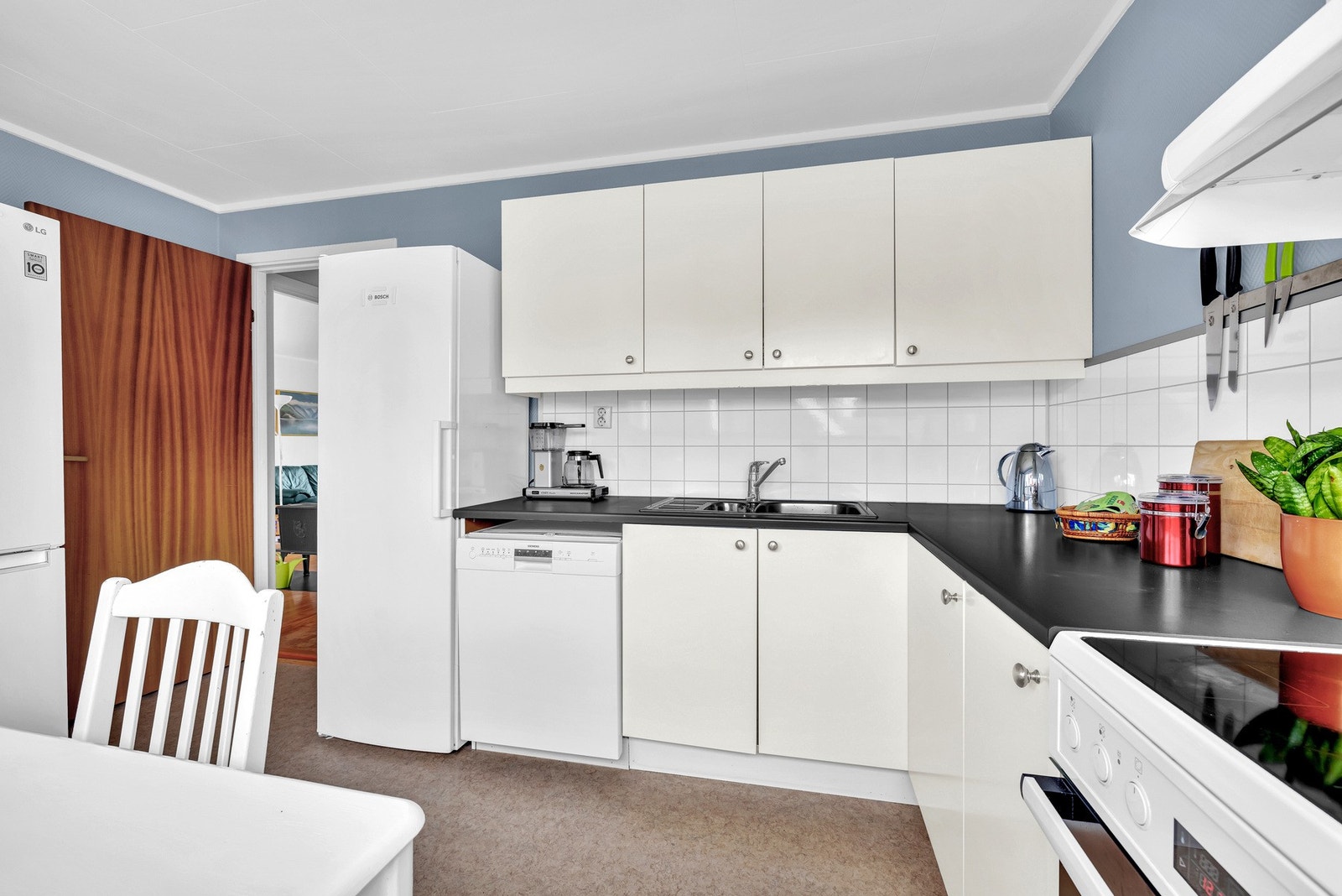 Det er fliser i sprutsonen mellom skap og benkeplate, samt nedfelt oppvaskkum i rustfritt stål med ett-greps armatur. Videre er kjøkkenet utstyrt med en frittstående komfyr med keramisk platetopp, frittstående kjøleskap og oppvaskmaskin. Galleribilde