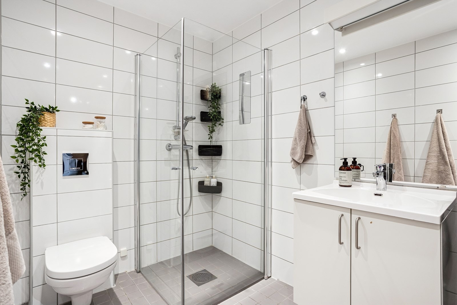 Badet er bestående av vegghengt toalett, dusjhjørne og servantskap med speil over. Galleribilde