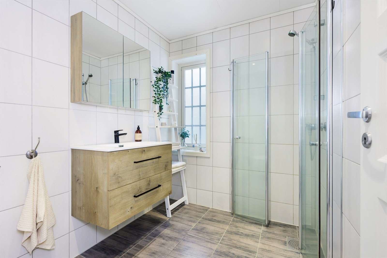 Badet i 1 etasje er helfliset og pent, med moderne innredning som vegghengt wc, dusjhjørne og servantinnredning med skuffer og speilskap. Galleribilde