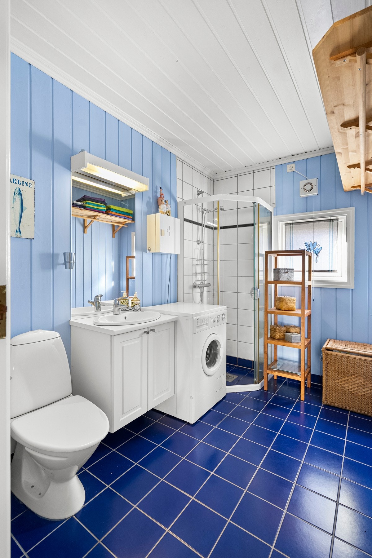 Badet har blå fliser på gulvet og lyseblå panelvegger. Galleribilde