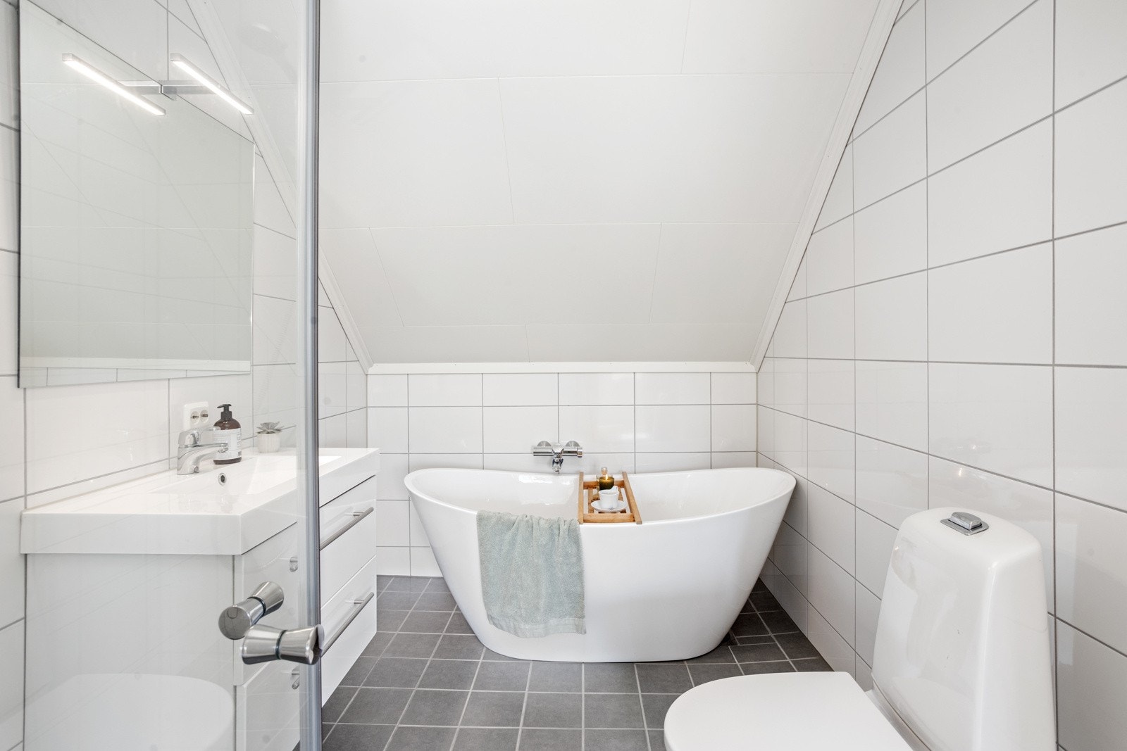 Badet er flislagt med varme i gulvet. Det er dusj med glassdører, toalett, servant over skuffeseksjon og et lekkert badekar. Galleribilde