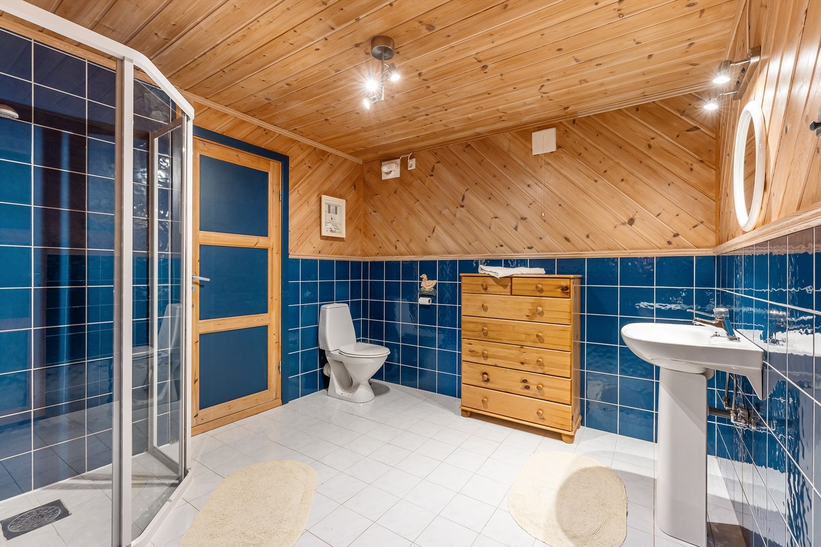 Romslig bad med delvis flislagte vegger og gulvvarme. Badet er innredet med gulvstående toalett, enkel servant og dusjhjørne med dusjgarnityr Galleribilde