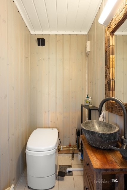 Praktisk innredet toalettrom med fliser på gulv og malt trepanel på vegg. Det er montert forbrenningstoalett. Galleribilde