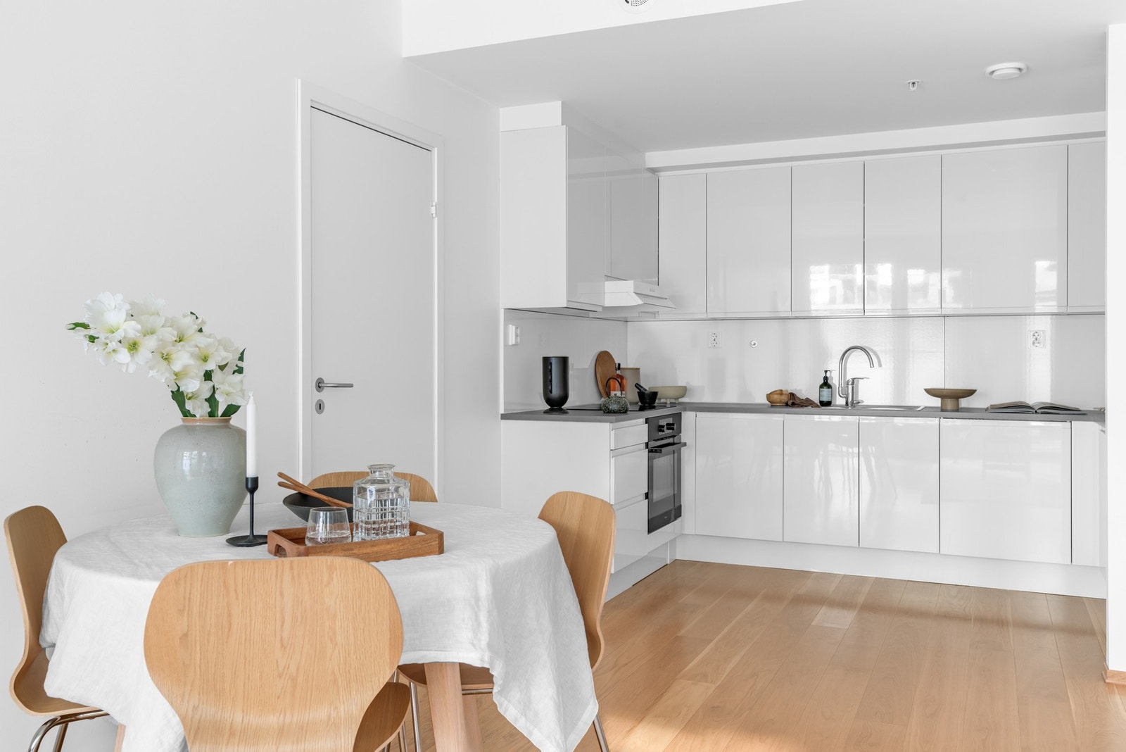 Det åpne og lyse kjøkkenet har tidløst, hvit innredning fra HTH med glatte, høyglans fronter og grå, laminert benkeplate med nedfelt kum i rustfritt stål. Galleribilde