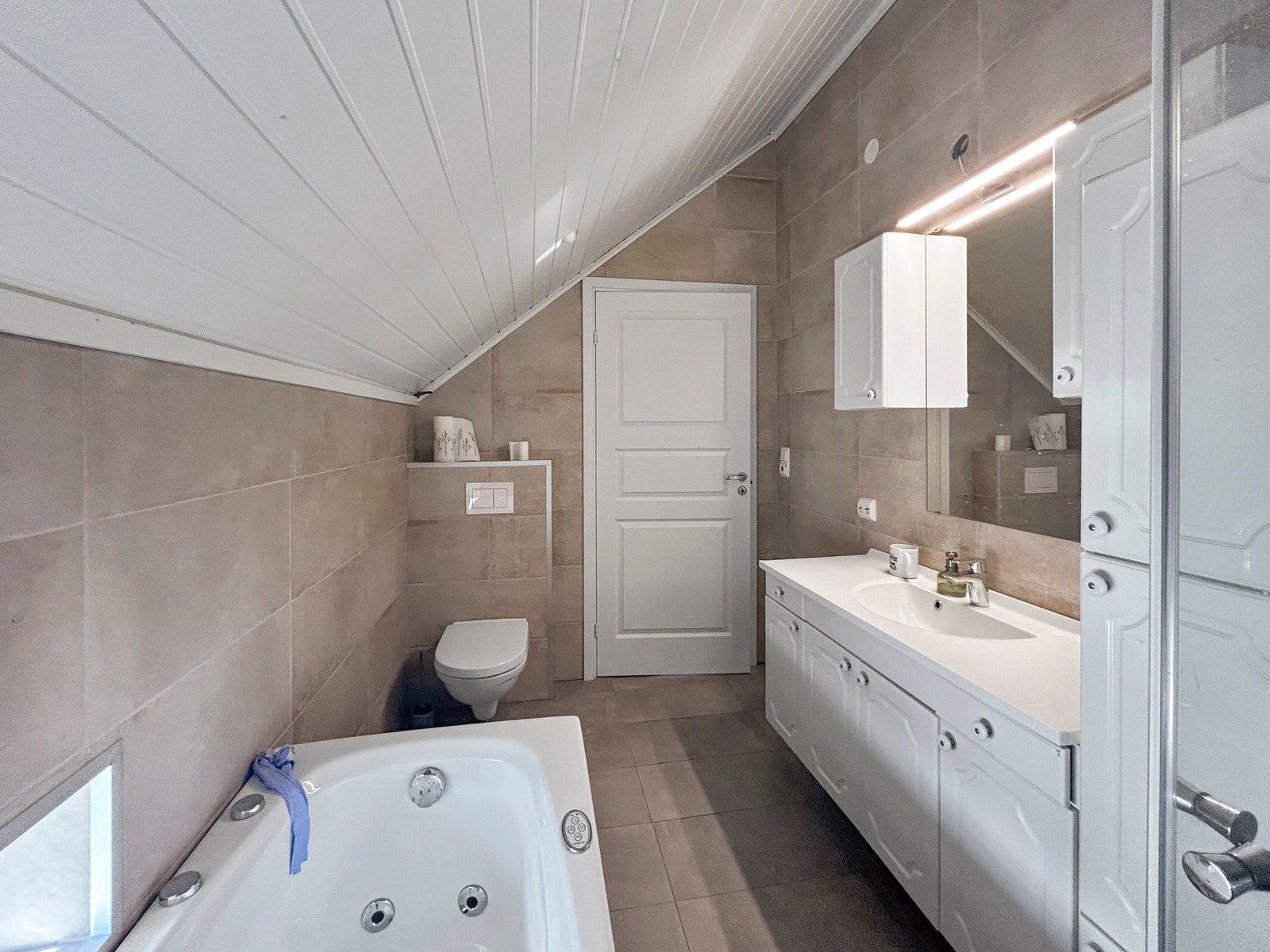 Moderne flislagt bad i lyse farger med dusjhjørne, badekar og baderomsinnredning med mye plass. Galleribilde