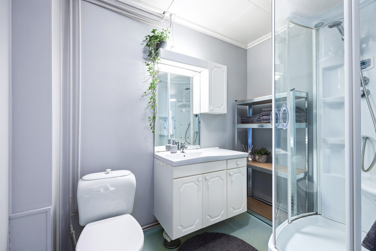 Bad med belegg på gulv og malte vegger og tak. Det er stråleovn på vegg og lys i tak. Badet har sanitærutstyr som toalett, vask og dusjkabinett. Galleribilde