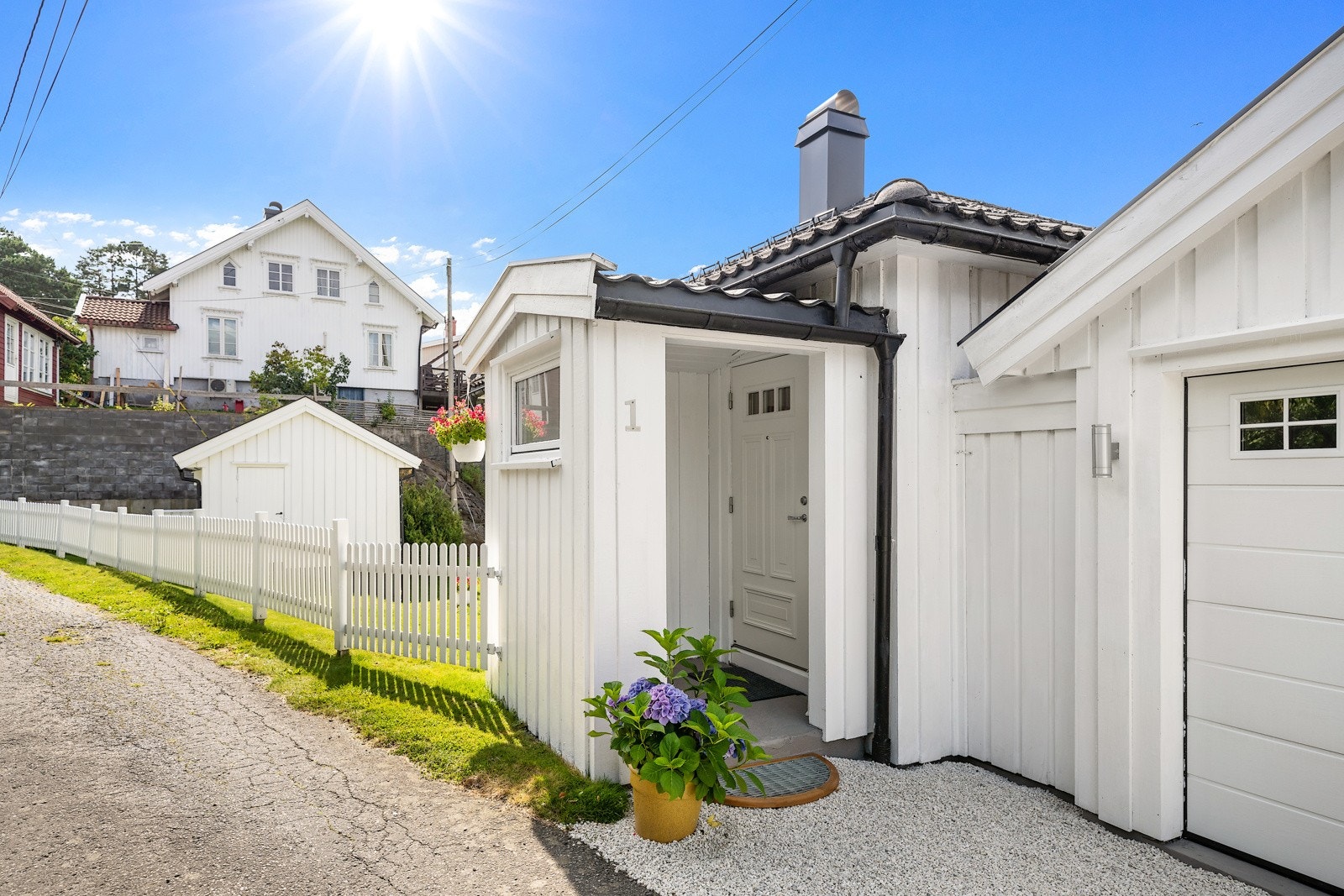 Hagen rammes pent inn av hvitmalt stakitt mot veien og har lys singel på gårdsplassen.Velkommen inn! Galleribilde