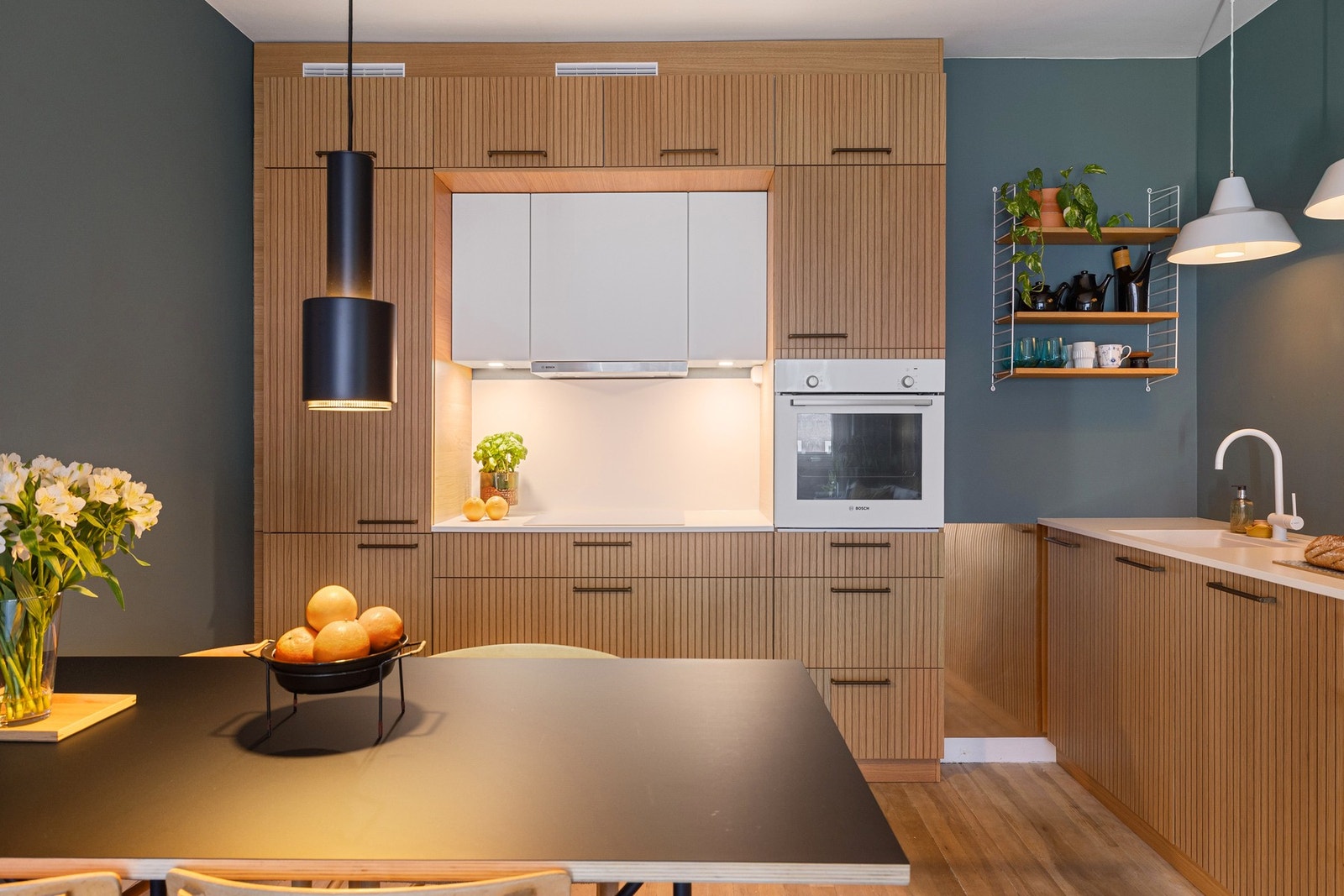 Fargepaletten i kjøkkenet holdes ren og ryddig, da induksjonstopp, vask og armatur fremstår som en del av benkeplaten. Galleribilde