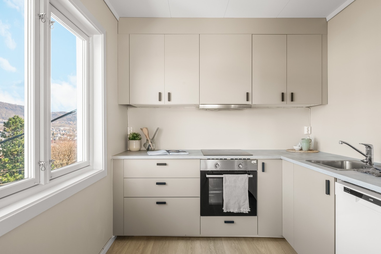 Lys og stilren kjøkkeninnredning med slette fronter og laminat benkeplate med stål vaskebeslag. Galleribilde