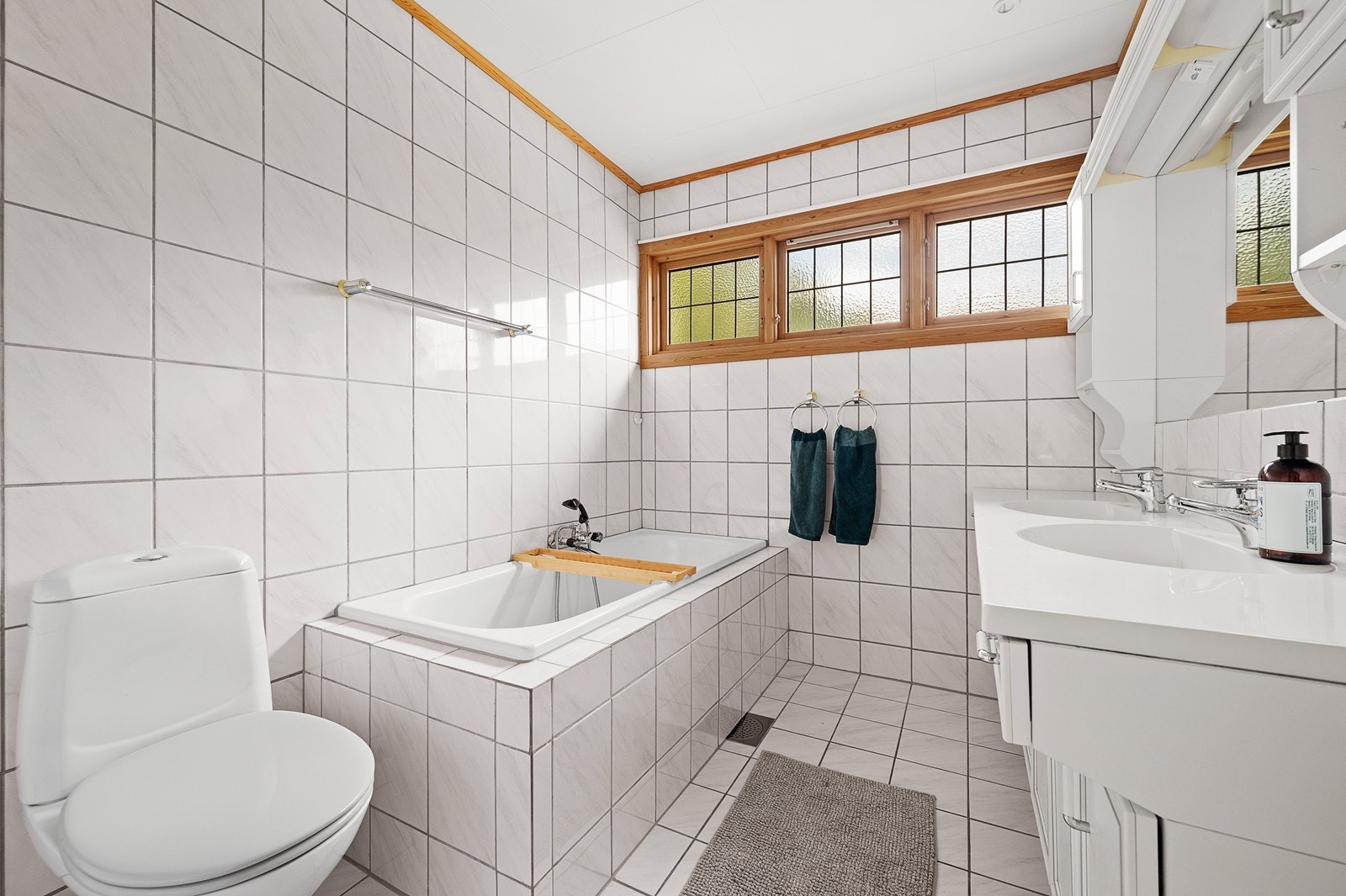 Badet i hovedetasjen har flislagt gulv og vegger og er utstyrt med badekar, toalett og servant med innredning Galleribilde