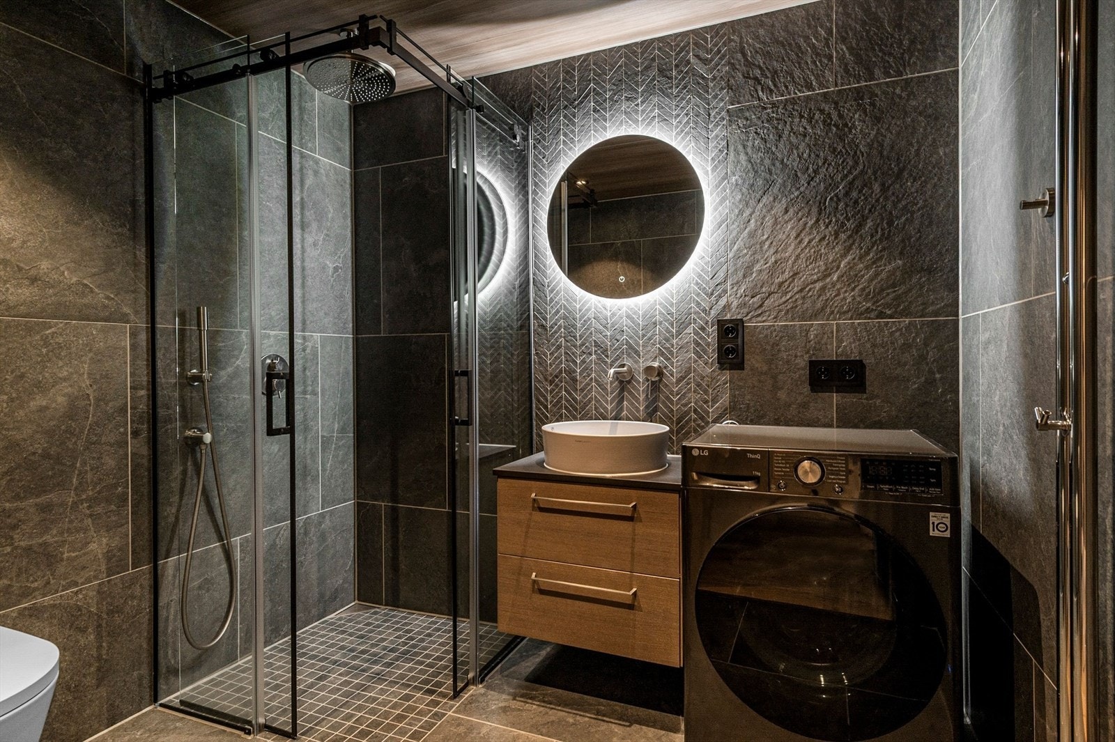 Hovedbad med dusjhjørne med glassdører, servant med underskap og speil med belysning. Opplegg for vaskemaskin og vegghengt toalett. Galleribilde