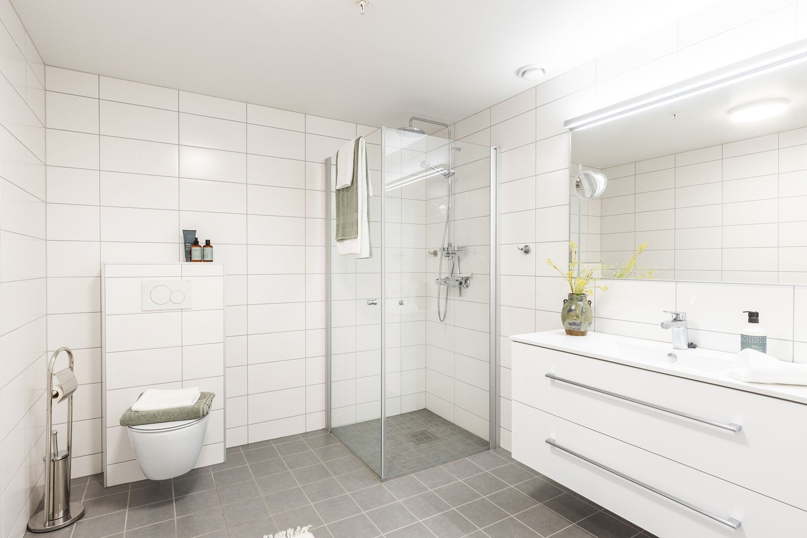 Det er god størrelse på badet som er flislagt, med vegghengt toalett, dusjnisje og innredning/speil med lys Galleribilde