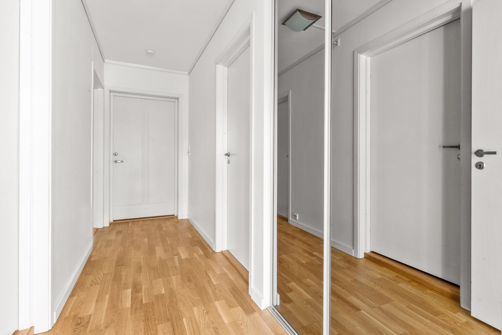 Praktisk gang med smart oppbevaringsløsning, inkludert skap skjult bak en elegant speil-skyvedør Galleribilde