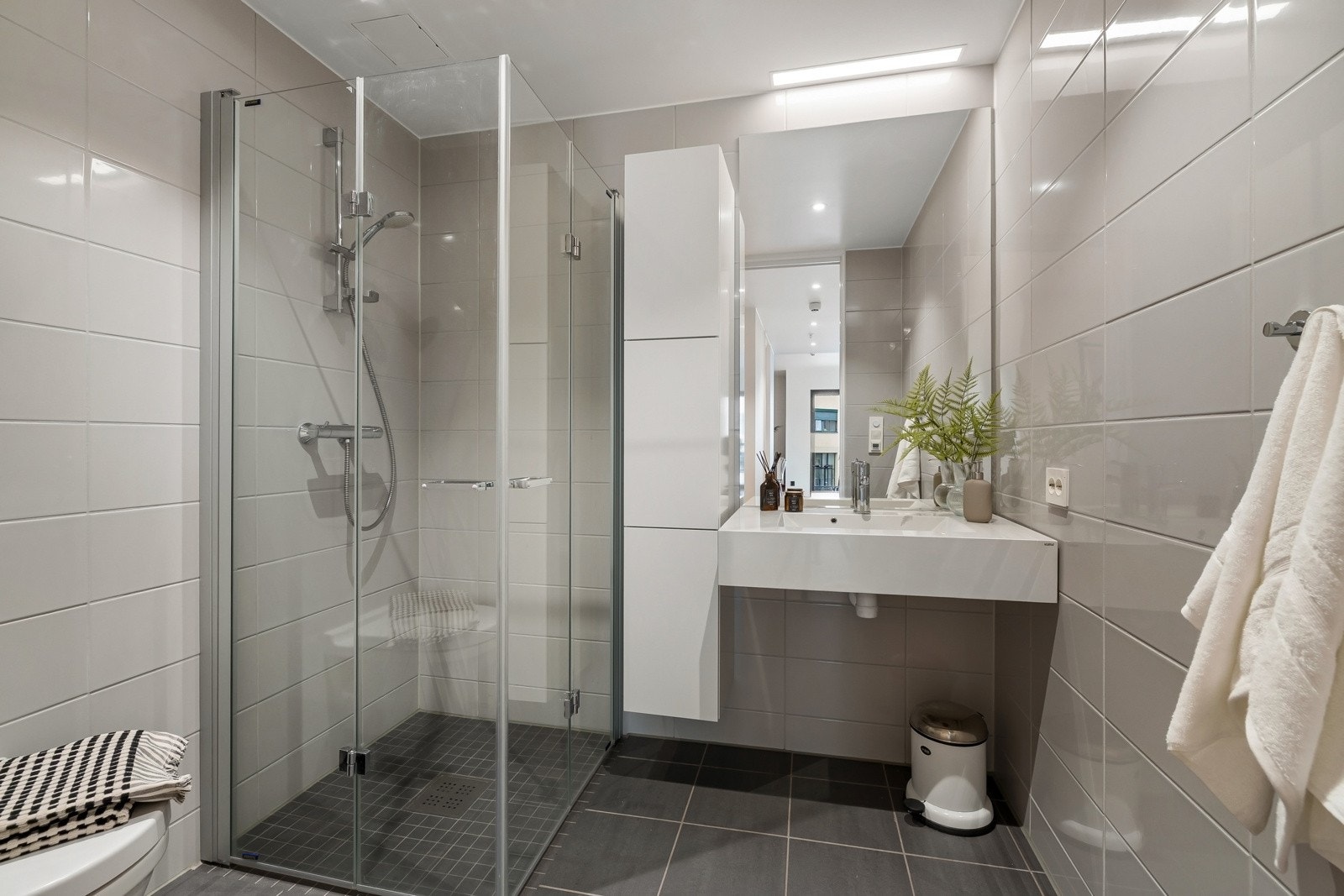 Baderom 1 - Flislagt bad/wc med varmekabler, avtrekk, speil, belysning, downlights, servant med innredning, dusj hjørne med innfellbare glassdører og vegghengt toalett. Galleribilde