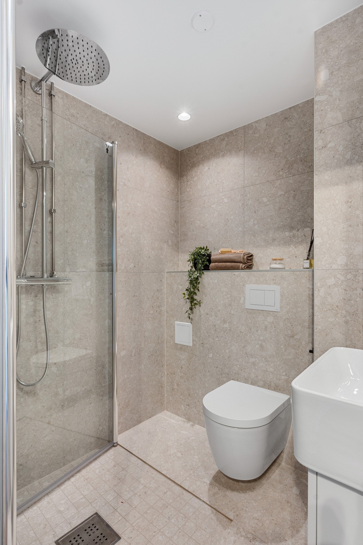 Badet er innredet med servantseksjon, speilskap, nedsenket dusjhjørne med glassdører og vegghengt toalett. Galleribilde