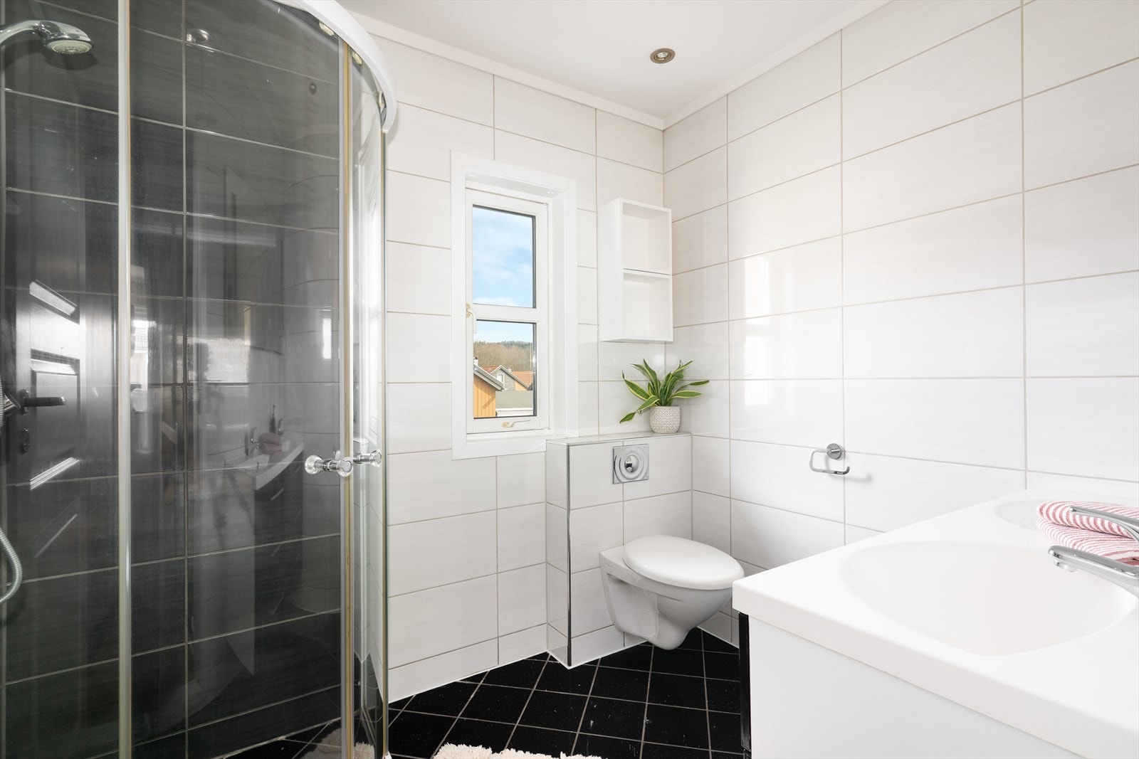 Badet er innredet med veggmontert toalett, dusjnisje med glassdører og servantinnredning med skuffer, servanter og speil med lys. Det er mekanisk avtrekk. Galleribilde