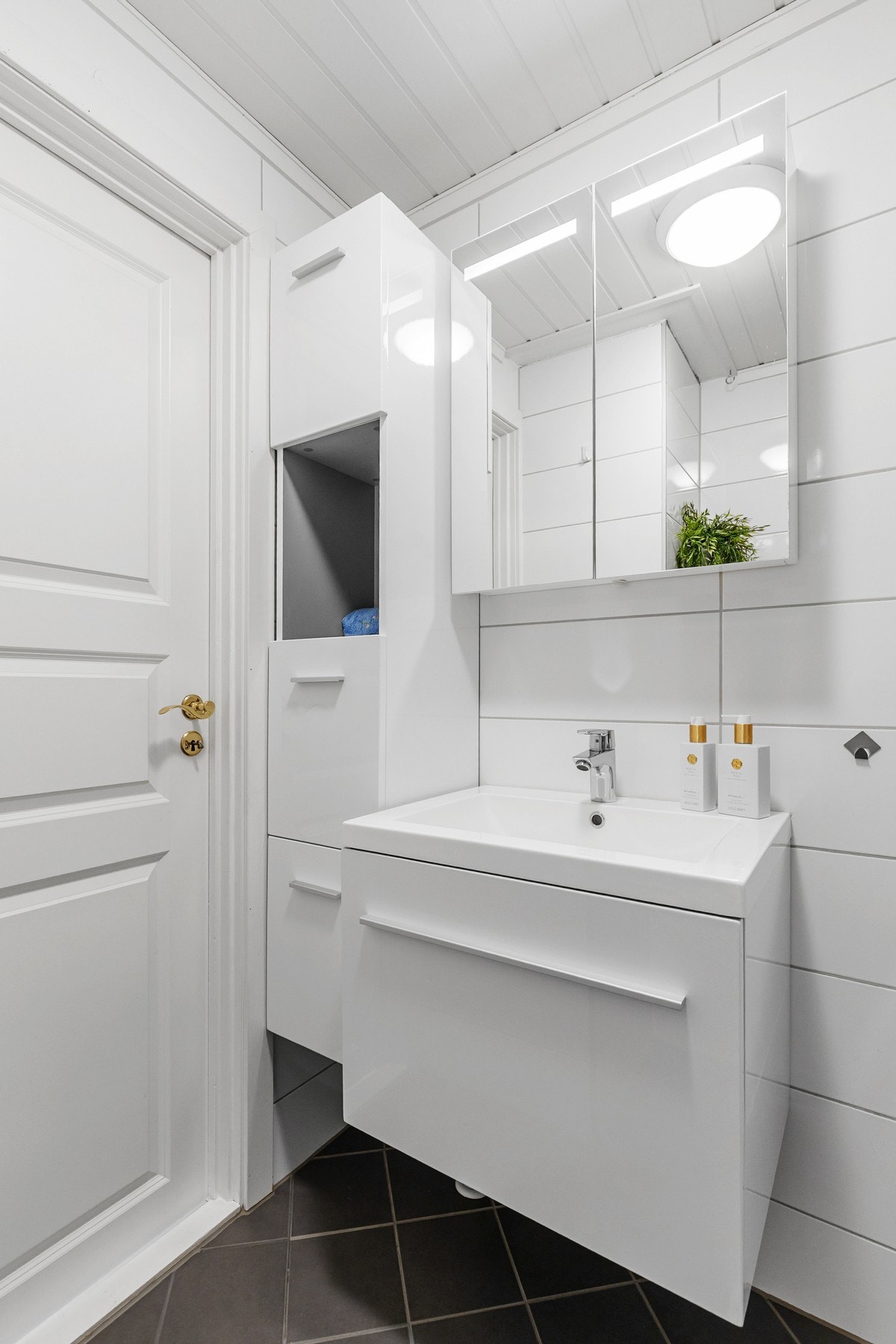 Rommet er innredet med dushjørne med innfellbare dører, hvit innredning med heldekkende servant og opplegg for vaskemaskin Galleribilde