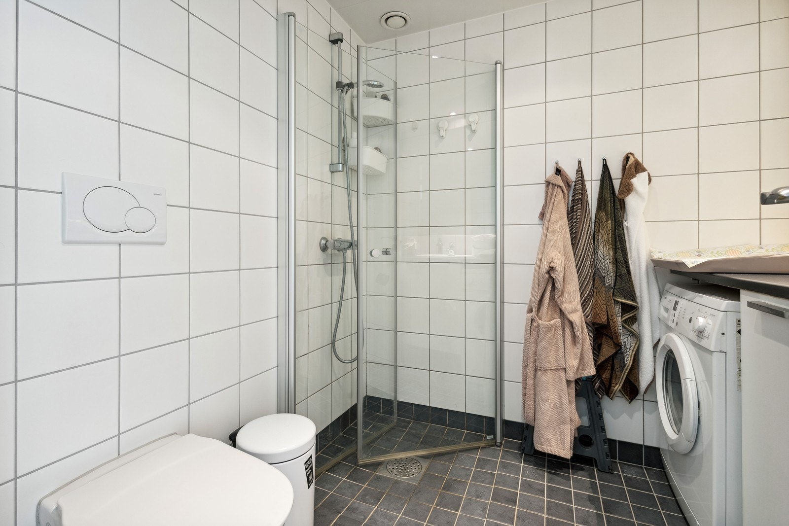 Flislagt bad, utstyrt med servant på innredning, dusjhjørne med glassdører og toalett. Galleribilde